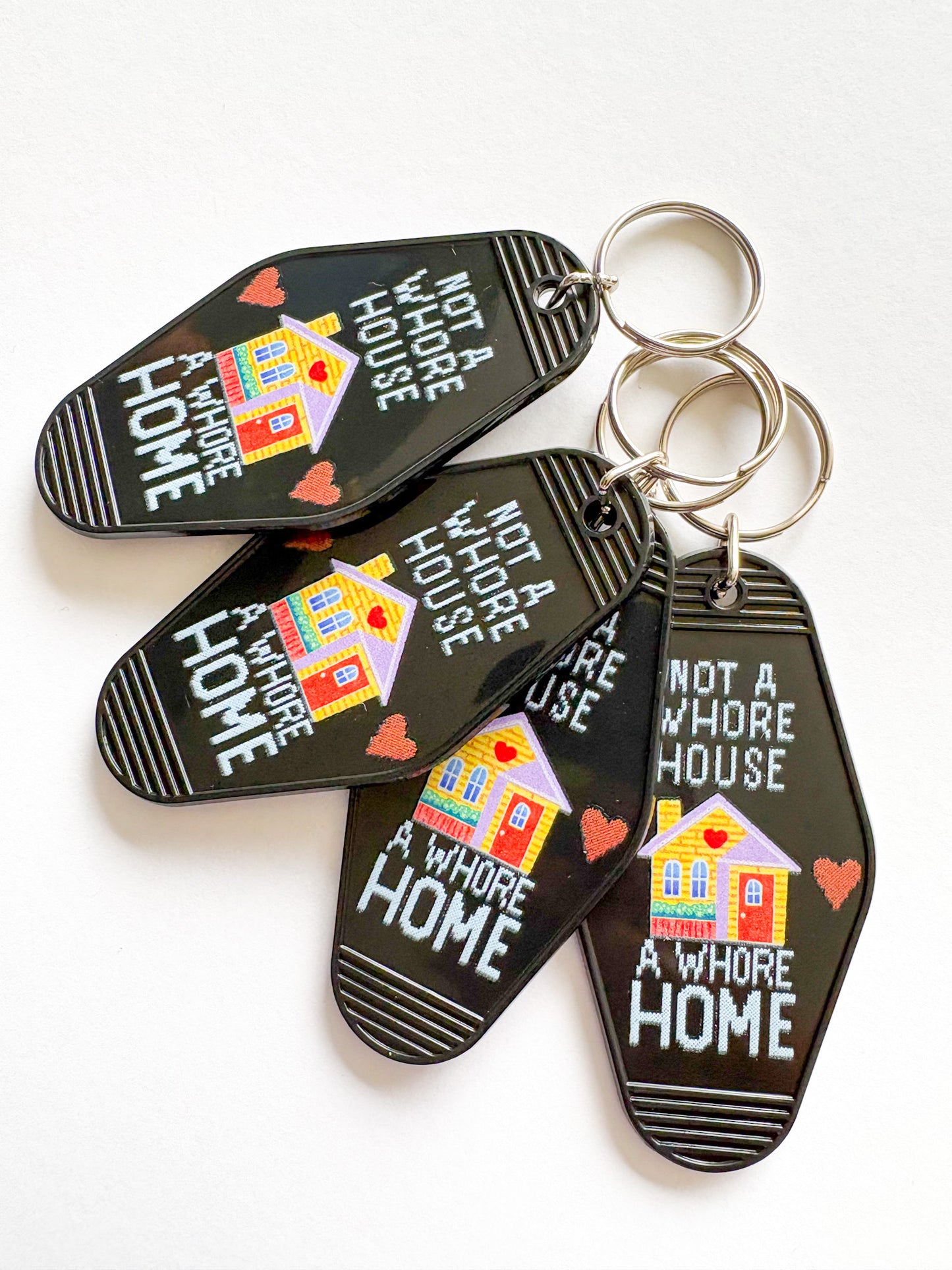 Set of keychains with 'Not a Whore House, A Whore Home' text and house illustrations on a white background.