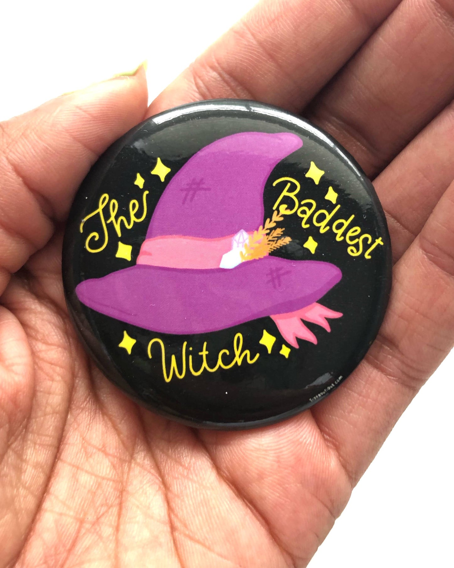 Button badge with purple witch hat design and text held in a hand