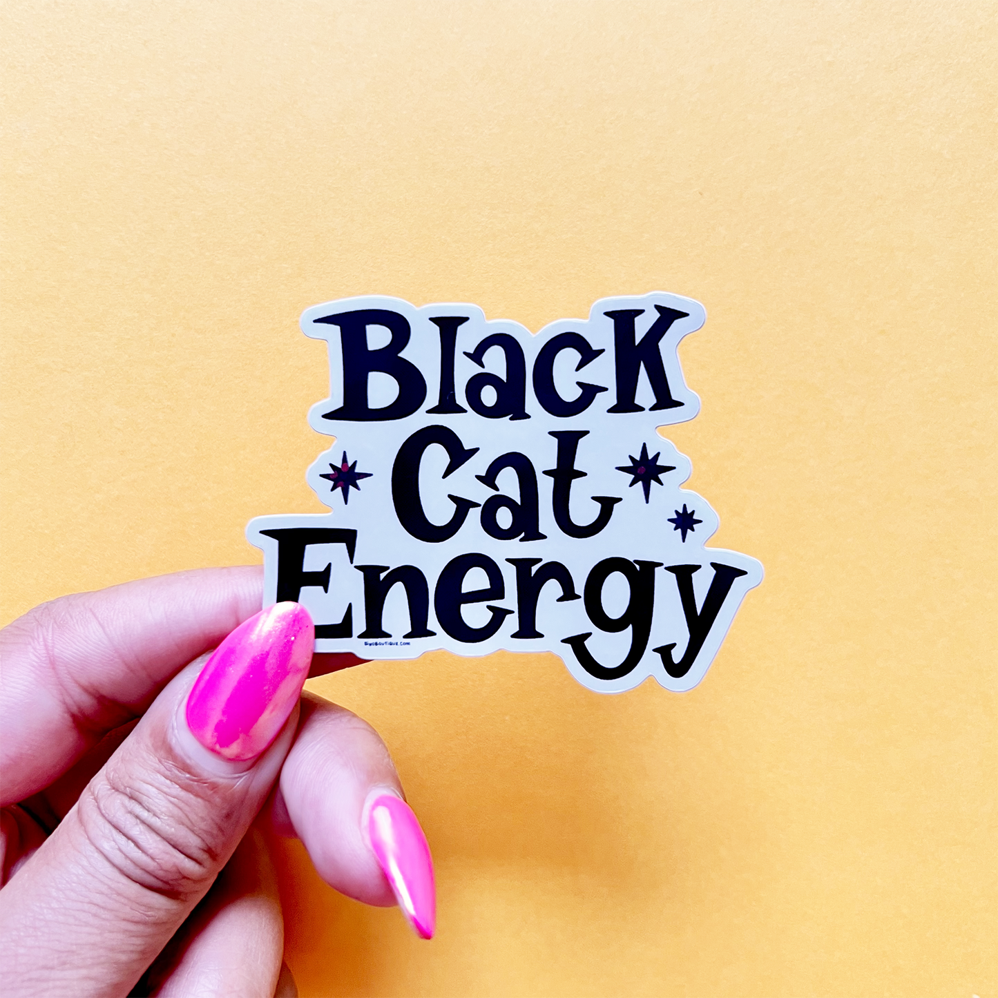 Sticker with 'Black Cat Energy' text held by a hand against a yellow background