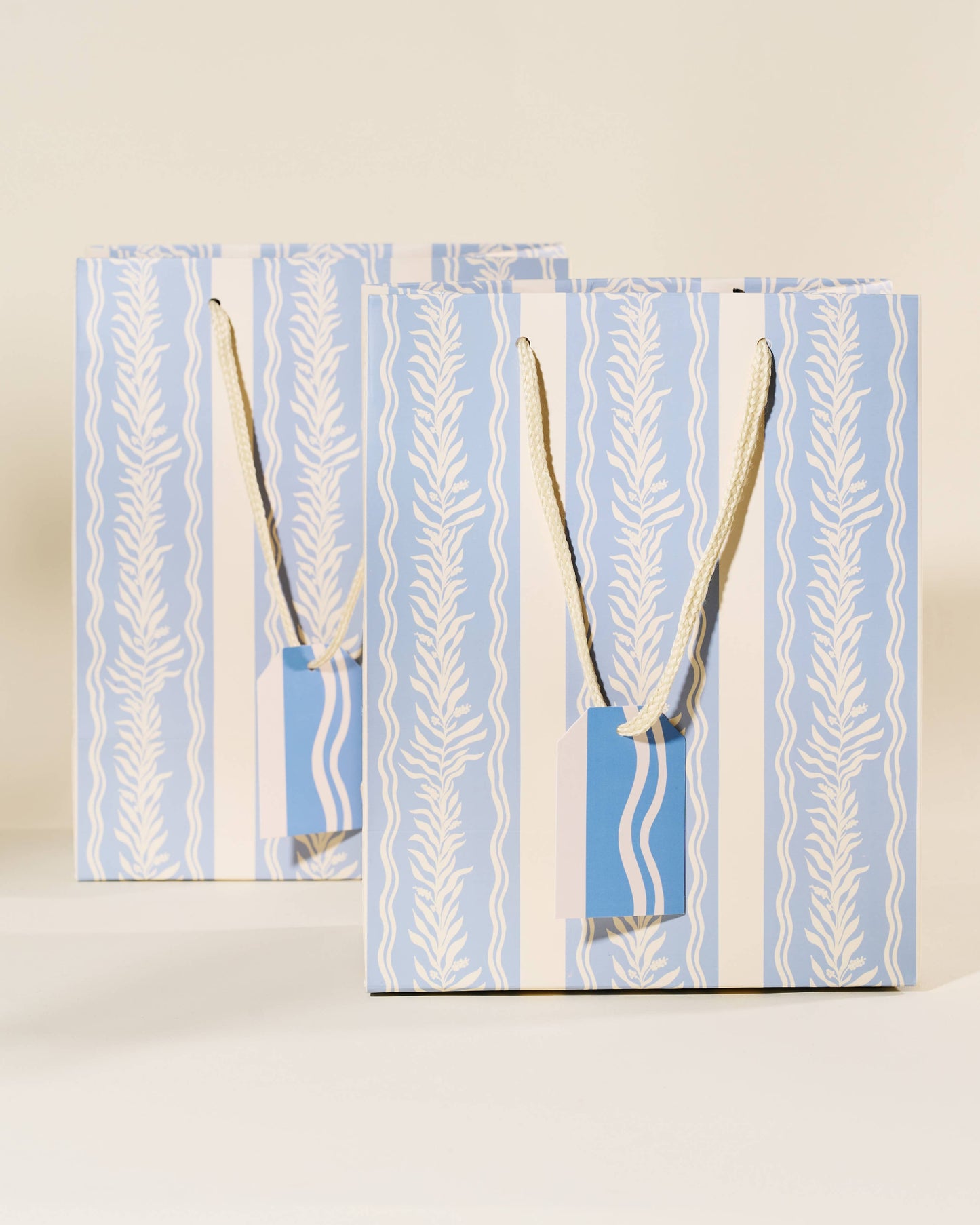 Two blue gift bags with white patterns and handles on a beige background, Blue Vine Medium Paper Gift Bag