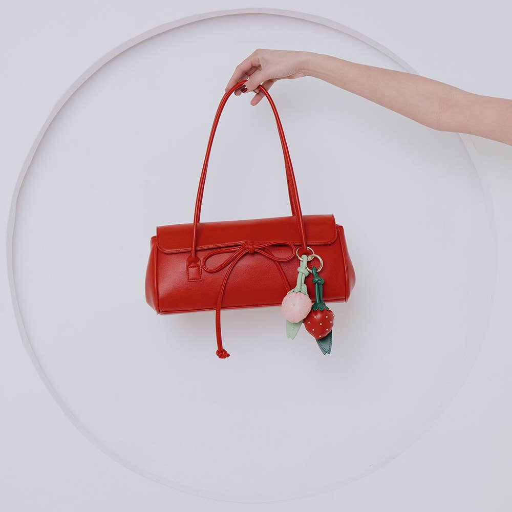 Red handbag with decorative charm held by a hand against a white, background, Bowie Shoulder Bag, Melie Bianco
