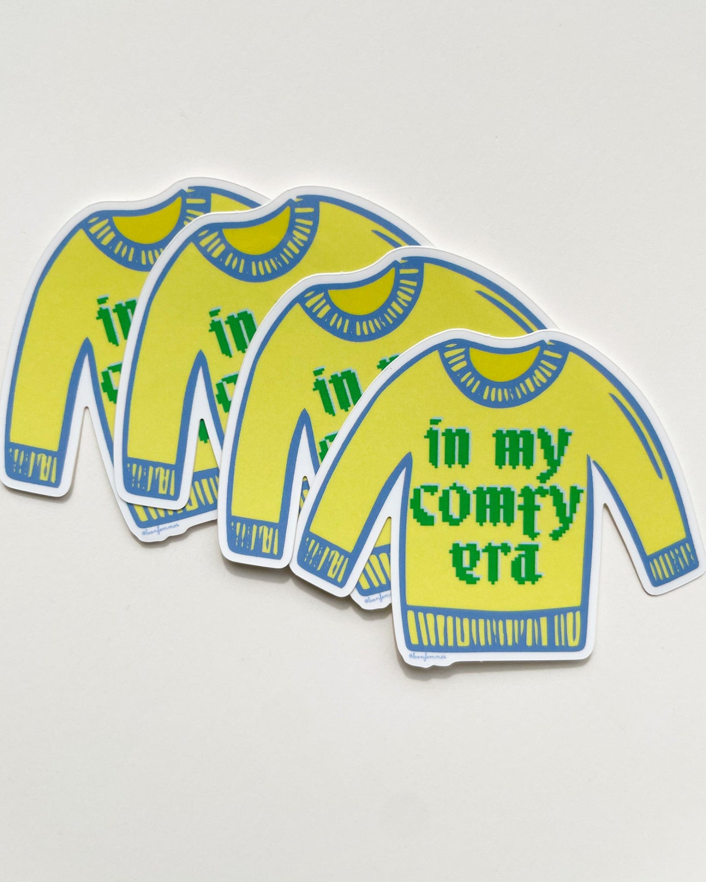Three yellow sweaters with blue trim and green text on a light gray, background Comfy Era Sweater Sticker Bon Femmes