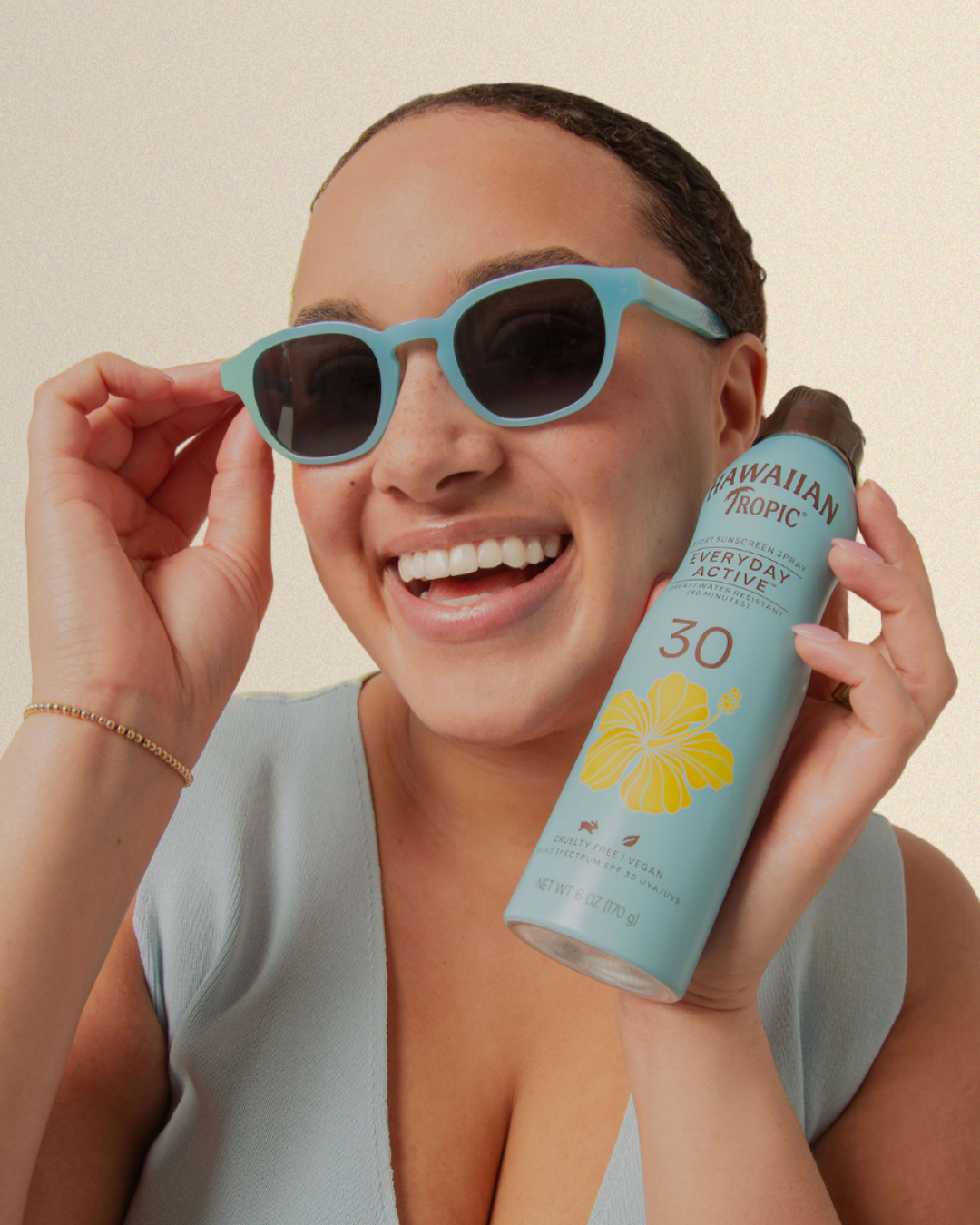 Woman wearing sunglasses and holding a can of Hawaiian Tropic sun lotion.
