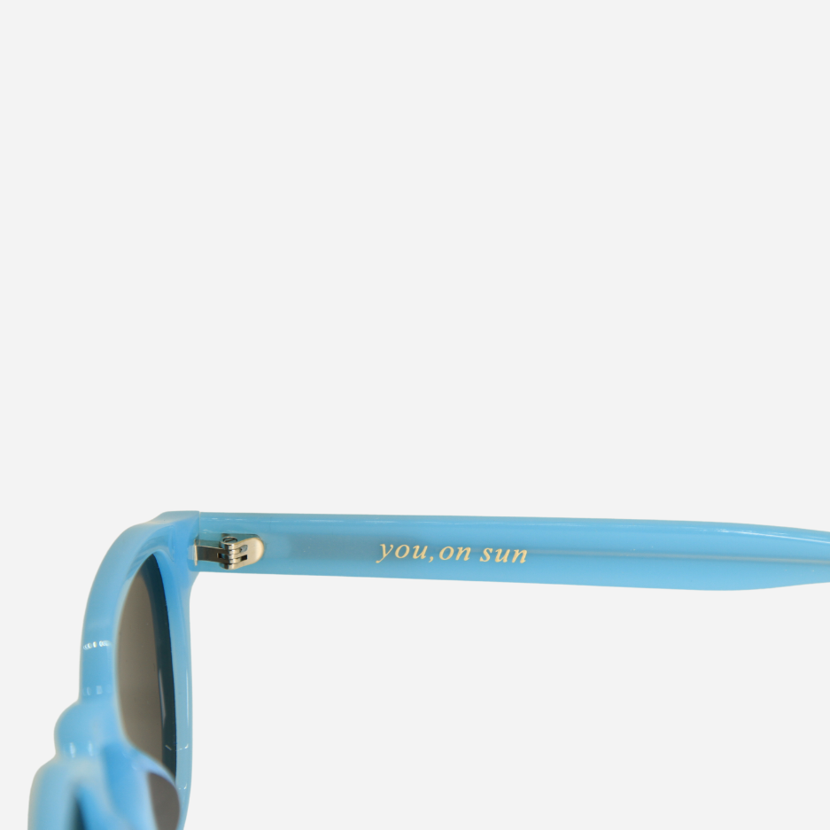 Close-up of a blue sunglasses with 'You ,on sun' text on the frame against a white background