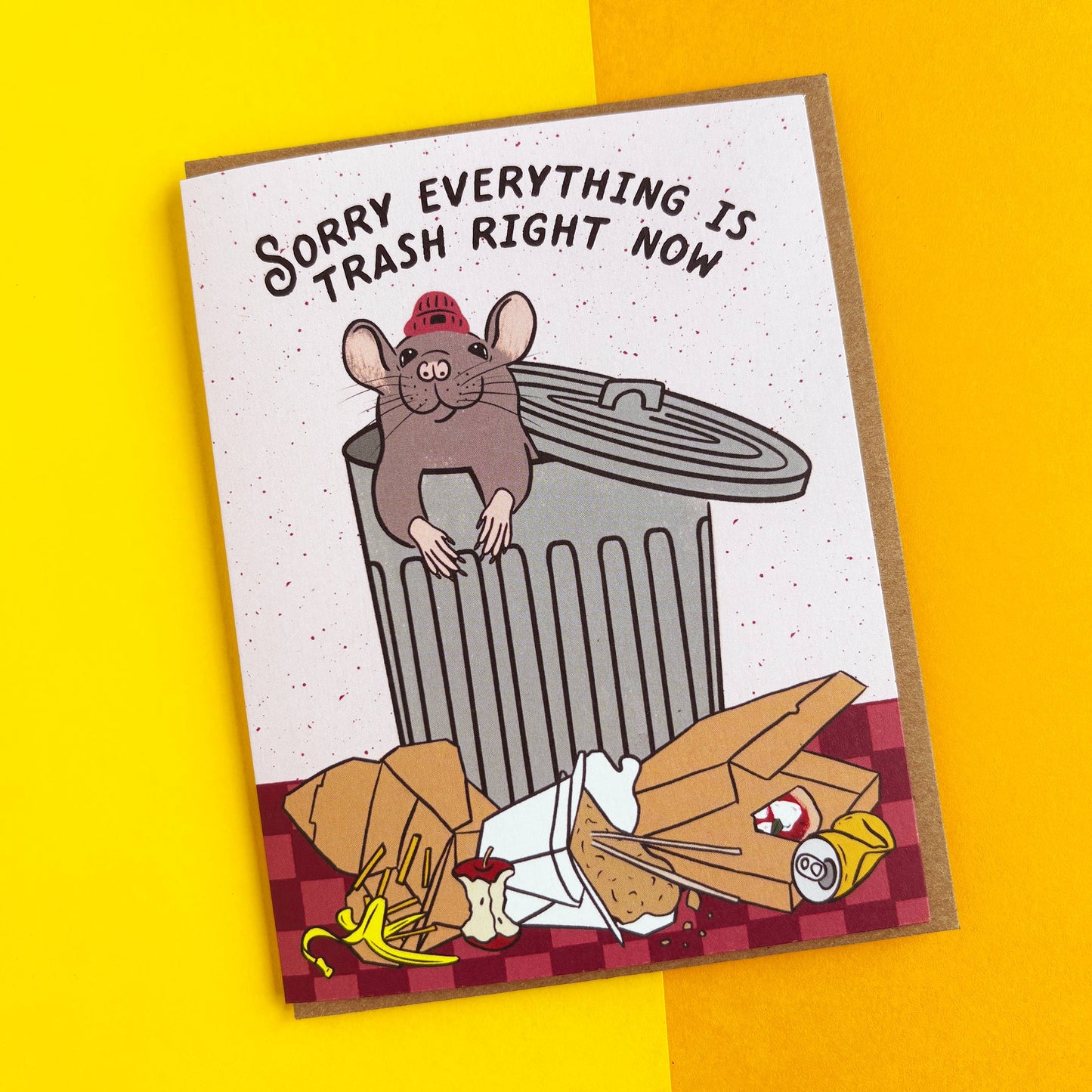 A rectangular novelty card or print with a cartoon mouse in a red firefighter helmet leaning on a trash can, with the text 'SORRY EVERYTHING IS TRASH RIGHT NOW' above. The card is photographed on a bright yellow background.