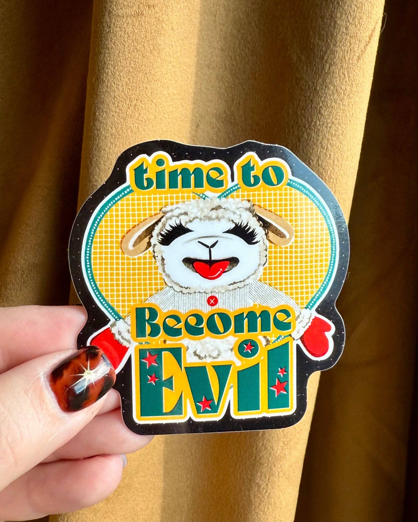 Sticker with a sheep design and text 'time to Become Evil' held against a beige background. Evil Lamb Chop Vinyl Sticker