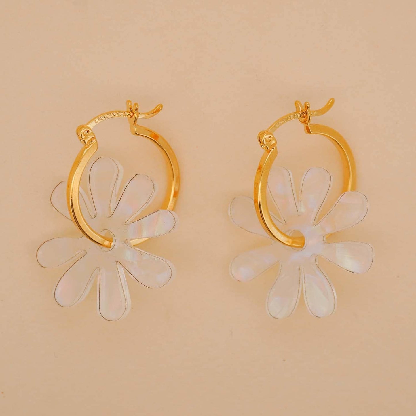 Gold hoop earrings with white floral designs on a beige background