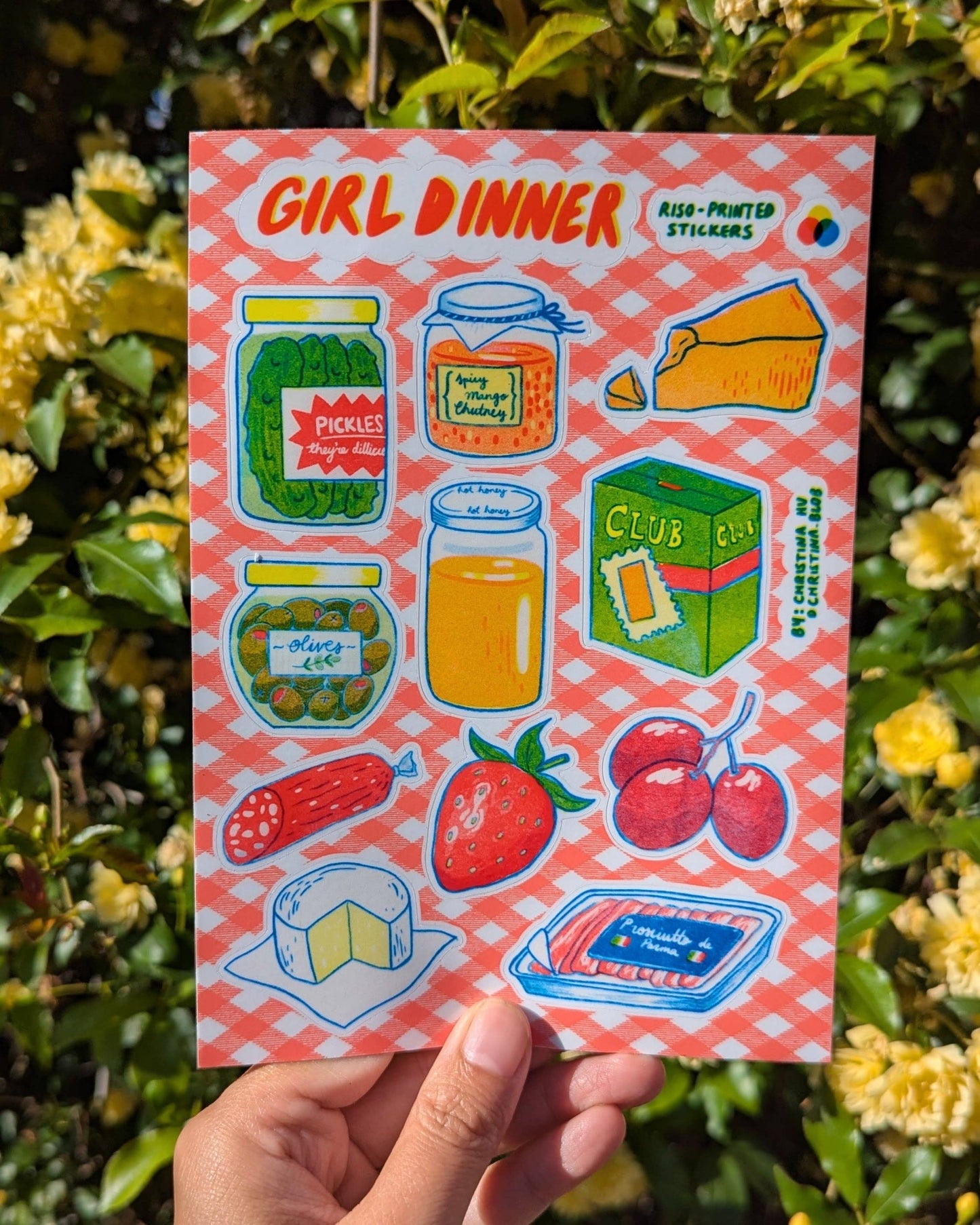 Sticker sheet titled 'Girl Dinner' held in front of a floral background, Girl Dinner Risograph Sticker Sheet