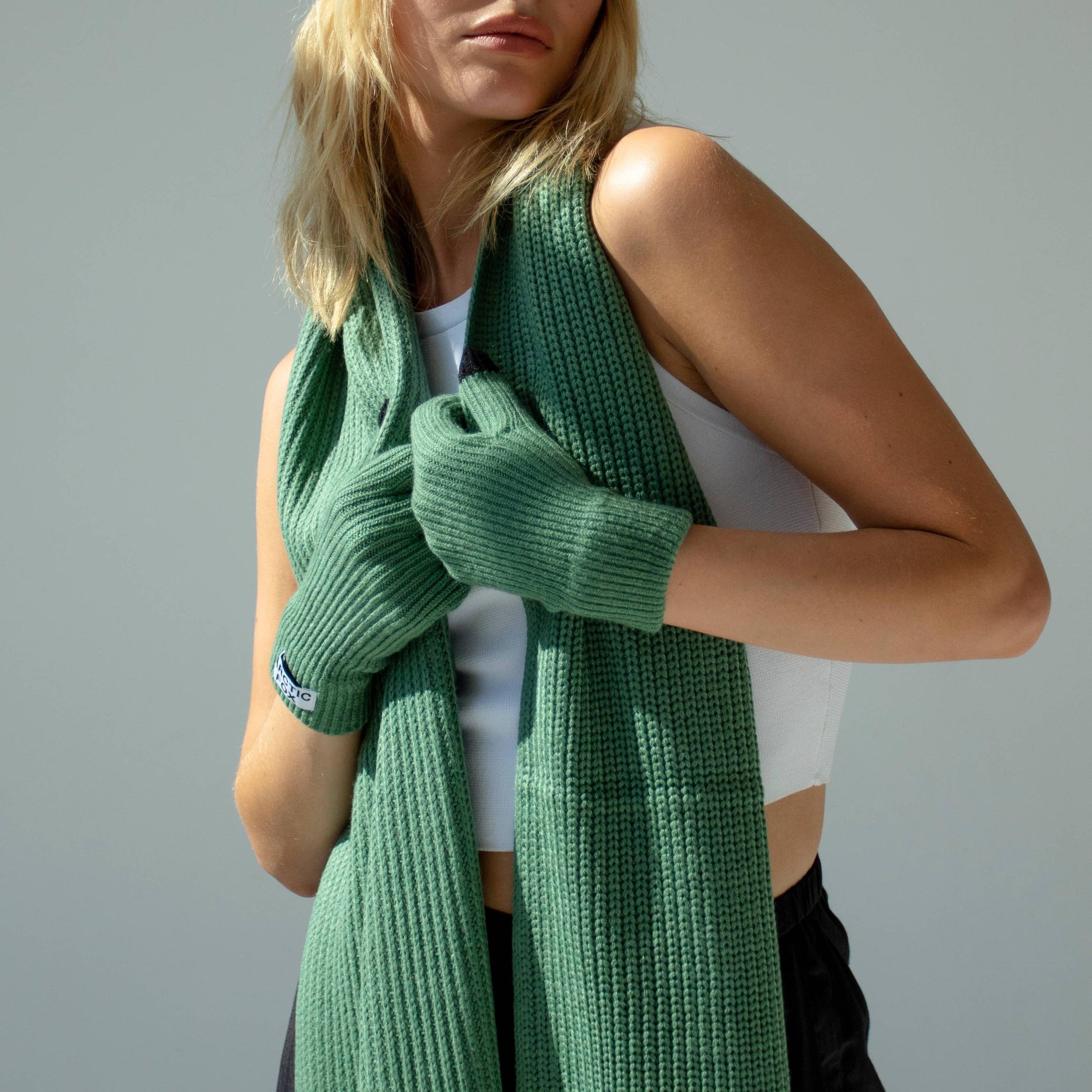Woman wearing a green knit beanie, scarf, and gloves against a gray background, Green Recycled Bottle Gloves