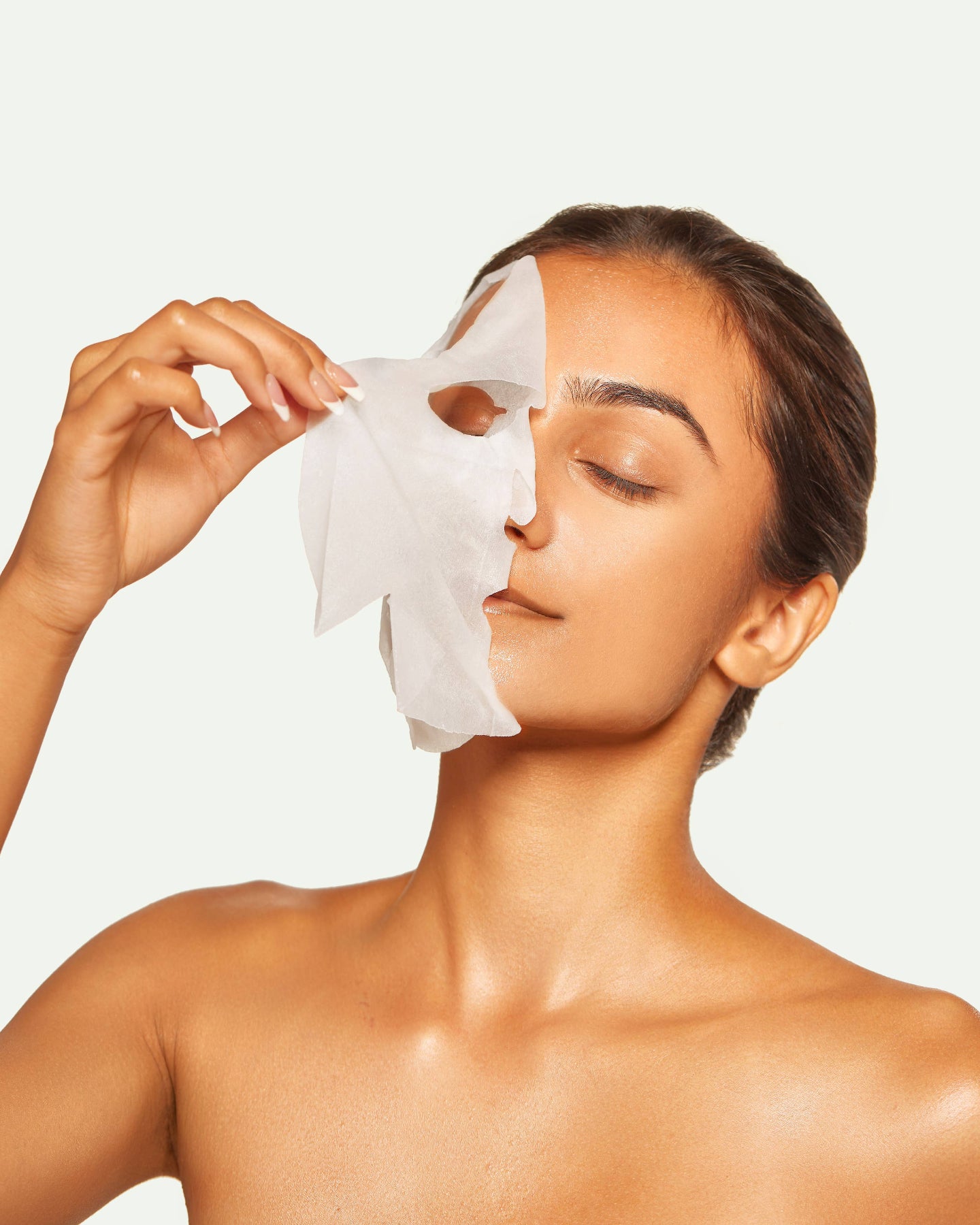 Woman applying a facial mask on a plain background, Green Reset Anti Aging Raw Juice Sheet Mask
