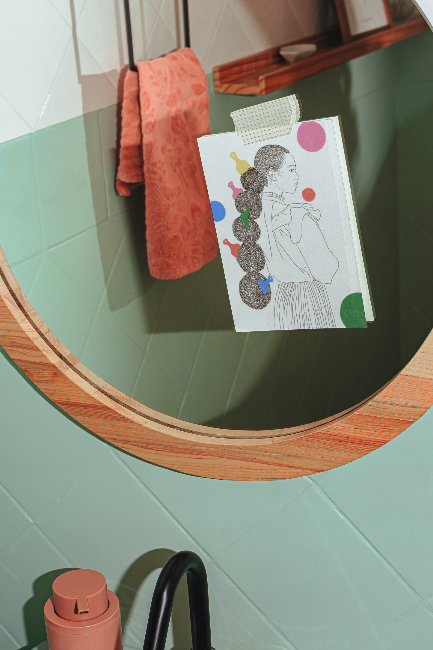 Round mirror with wooden frame on a light green wall, featuring a card with a colorful design.