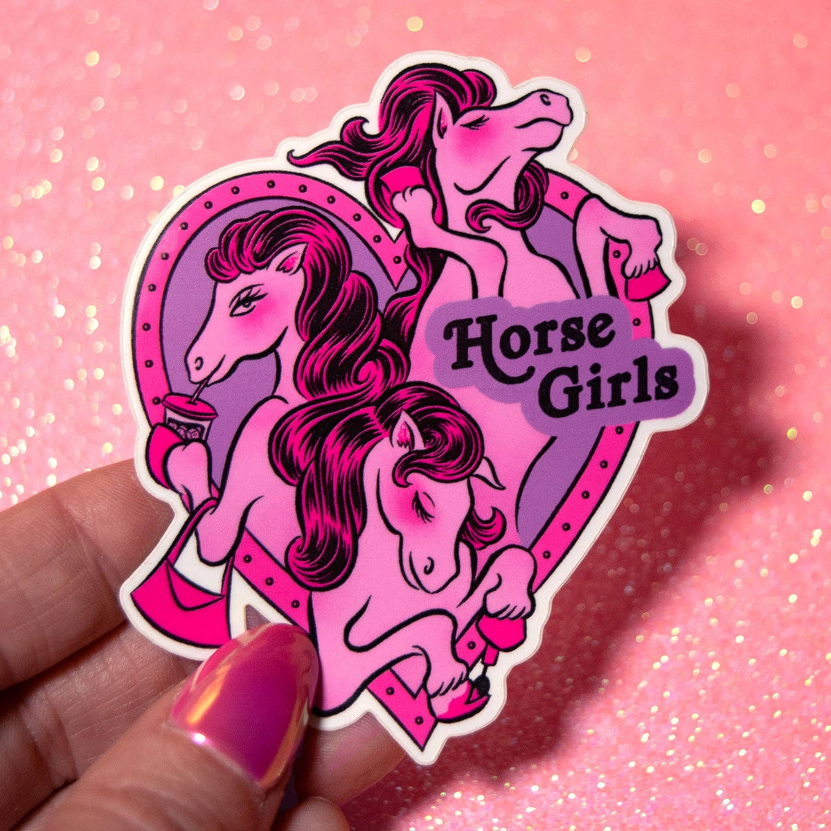 A hand holds a die-cut sticker featuring three illustrated pink and purple horses with the words 'Horse Girls' on a glittery pink background.