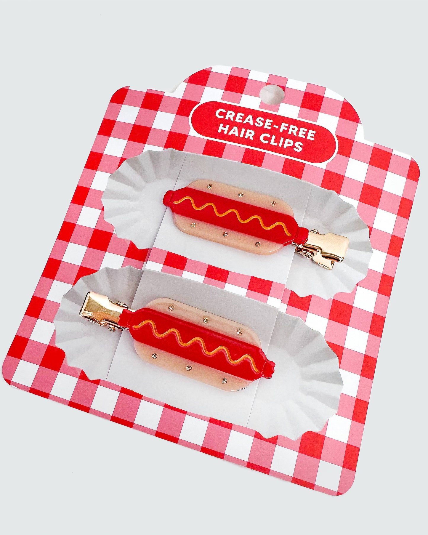Hot dog-shaped hair clips in a red and white checkered package on a light gray background