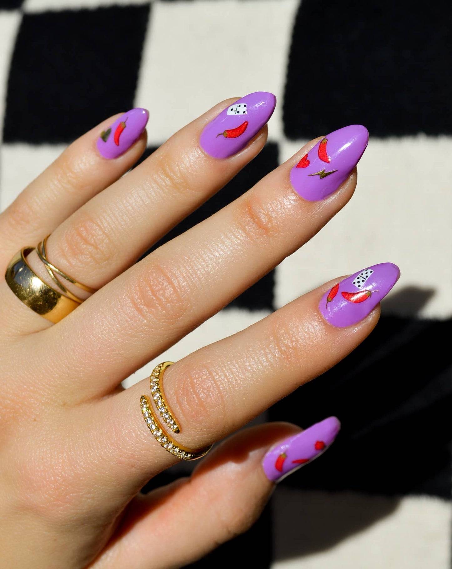 Hand with purple nail art featuring small decorative elements on a checkered background