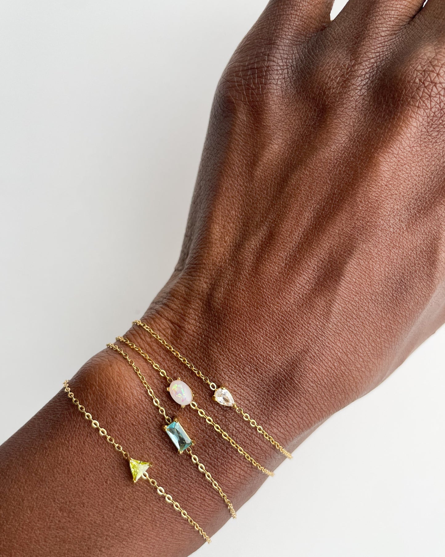 Hand wearing multiple gold bracelets with gemstone accents on a light background