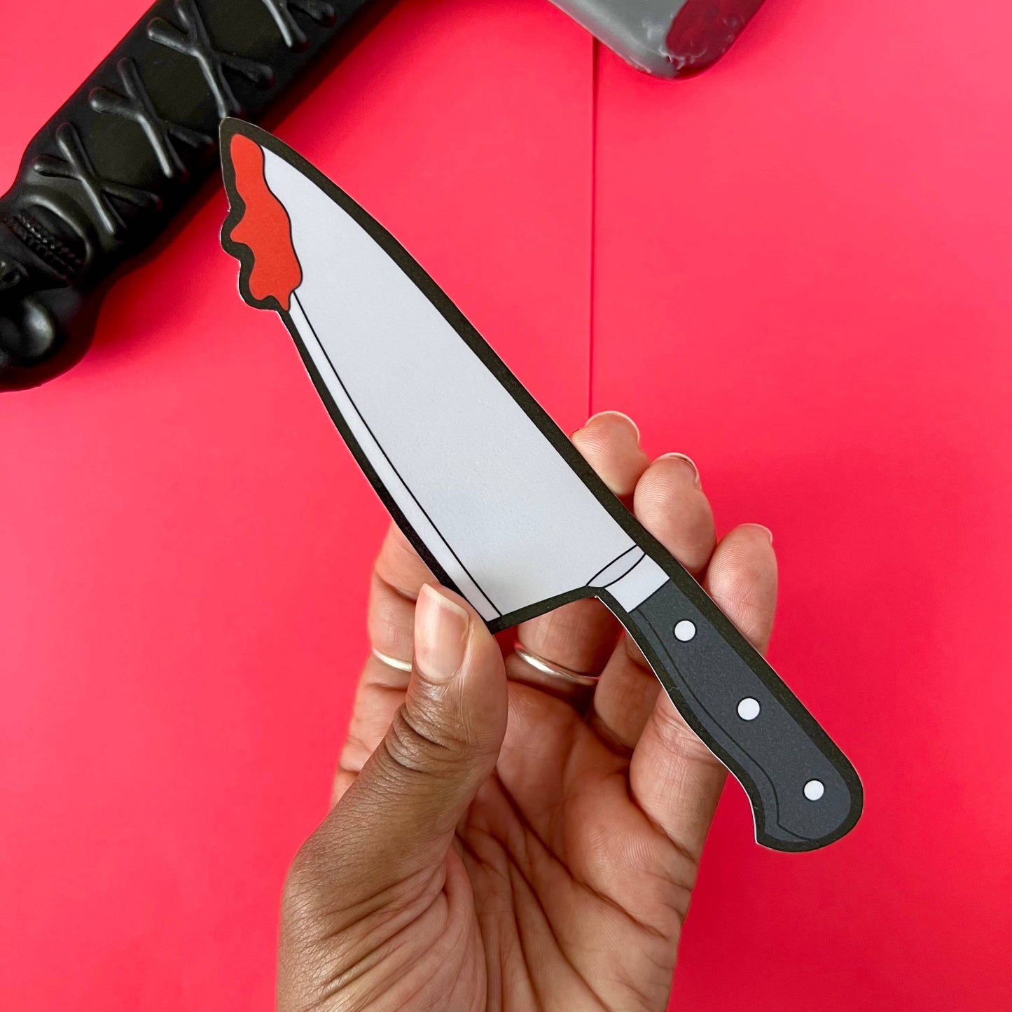 Hand holding a knife bookmark with a red blade against a red background