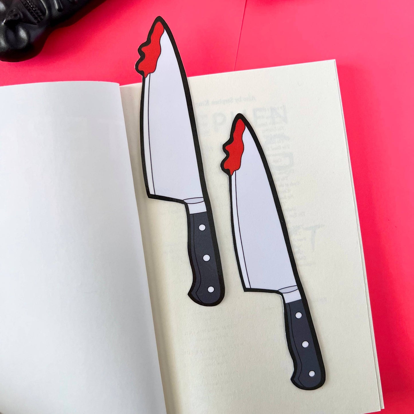 Two knife bookmarks with blood effects on a white book against a red background