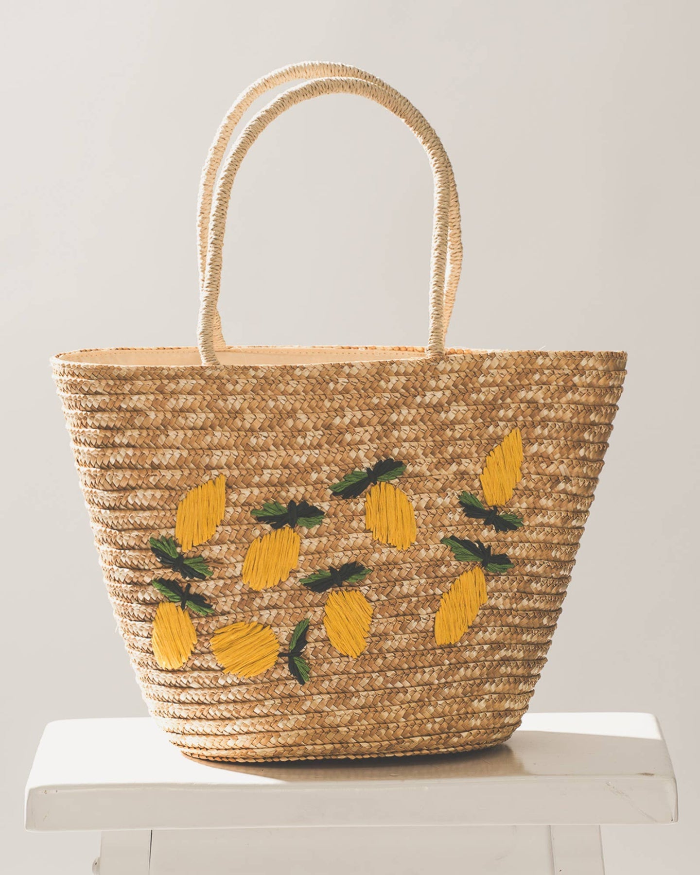 Woven bag with lemon designs on a white stool against a light gray background