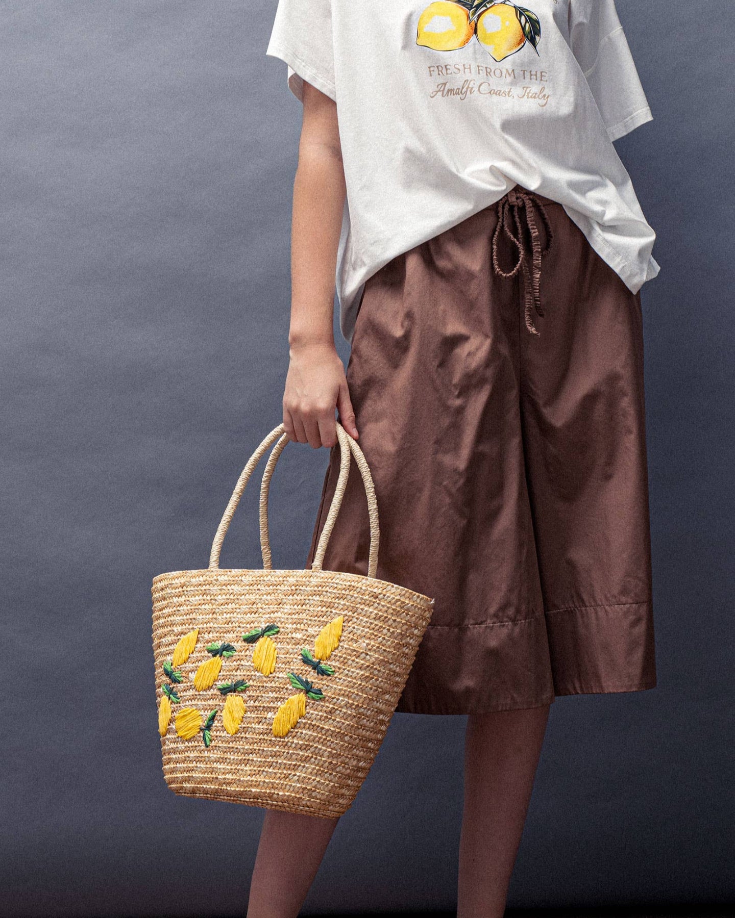Person holding a straw bag with lemon designs against a plain background