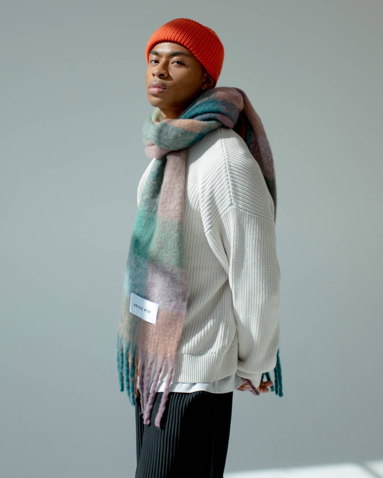 Person wearing a colorful scarf and red beanie against a plain background, Lilac Check Recycled Bottle Reykjavik Scarf