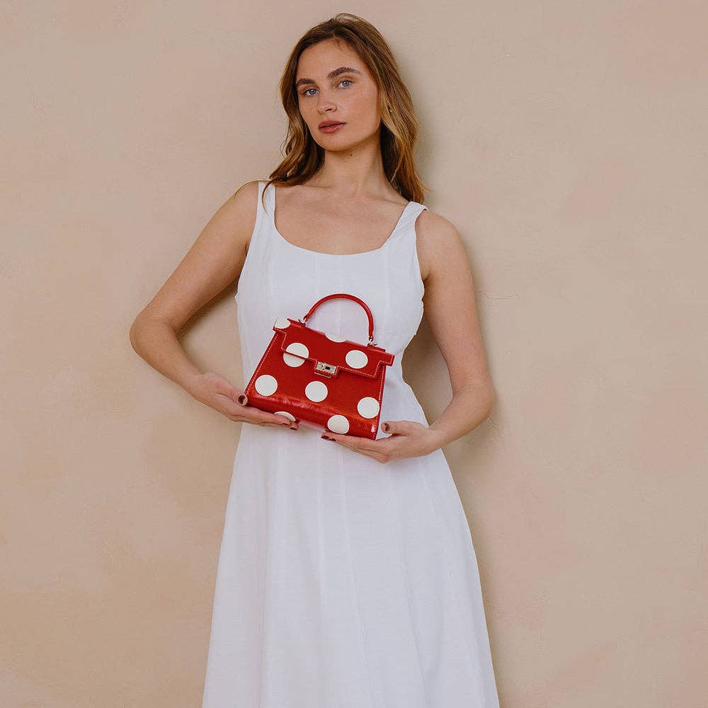 Woman holding a red handbag with white polka dots against a beige background