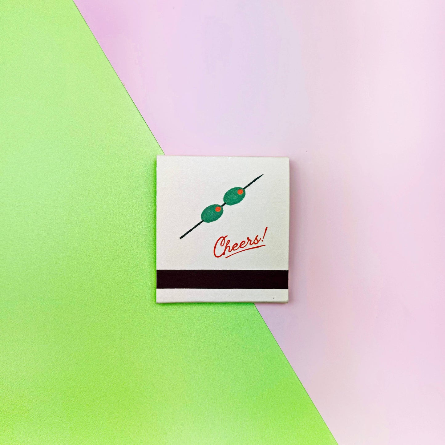 Matchbook with skewer and 'Cheers!' text on a green and pink gradient background. Martini Matches