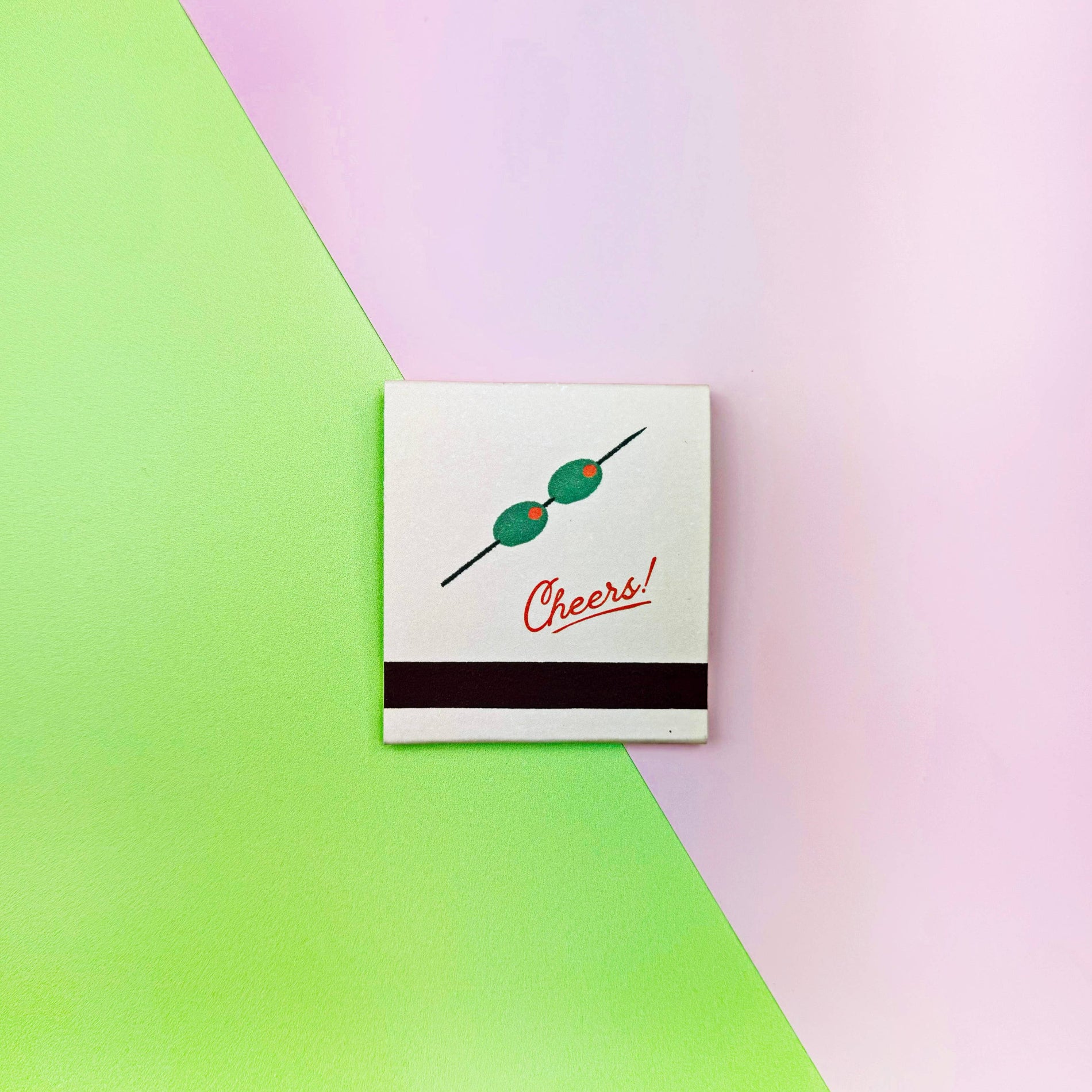 Matchbook with skewer and 'Cheers!' text on a green and pink gradient background. Martini Matches