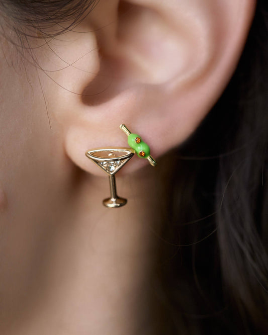 Close-up of an ear wearing a cocktail glass earring with a green olive.