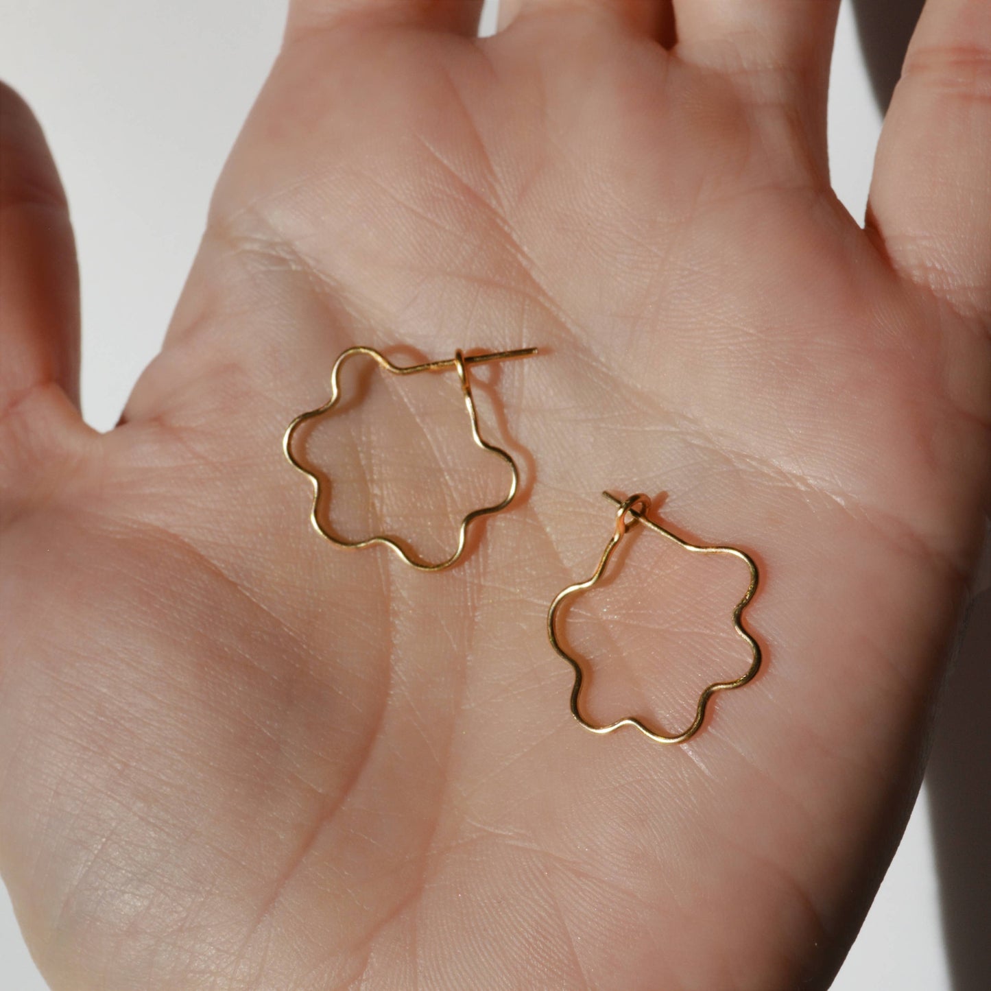 Gold flower-shaped earrings held in a hand against a neutral background, Mini Flora Hoop Earrings in Gold