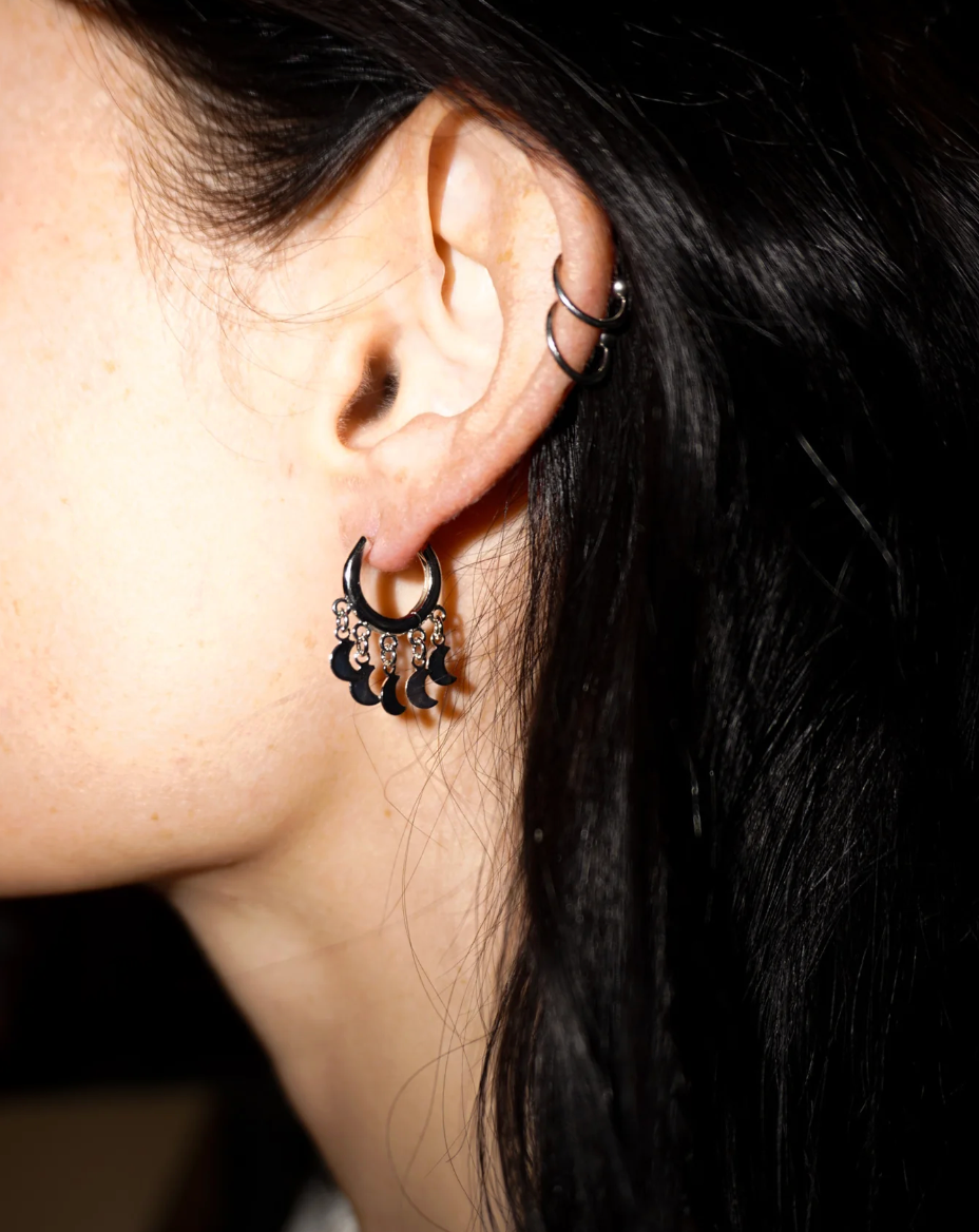 Close-up of an ear with black dangling earrings and a dark background