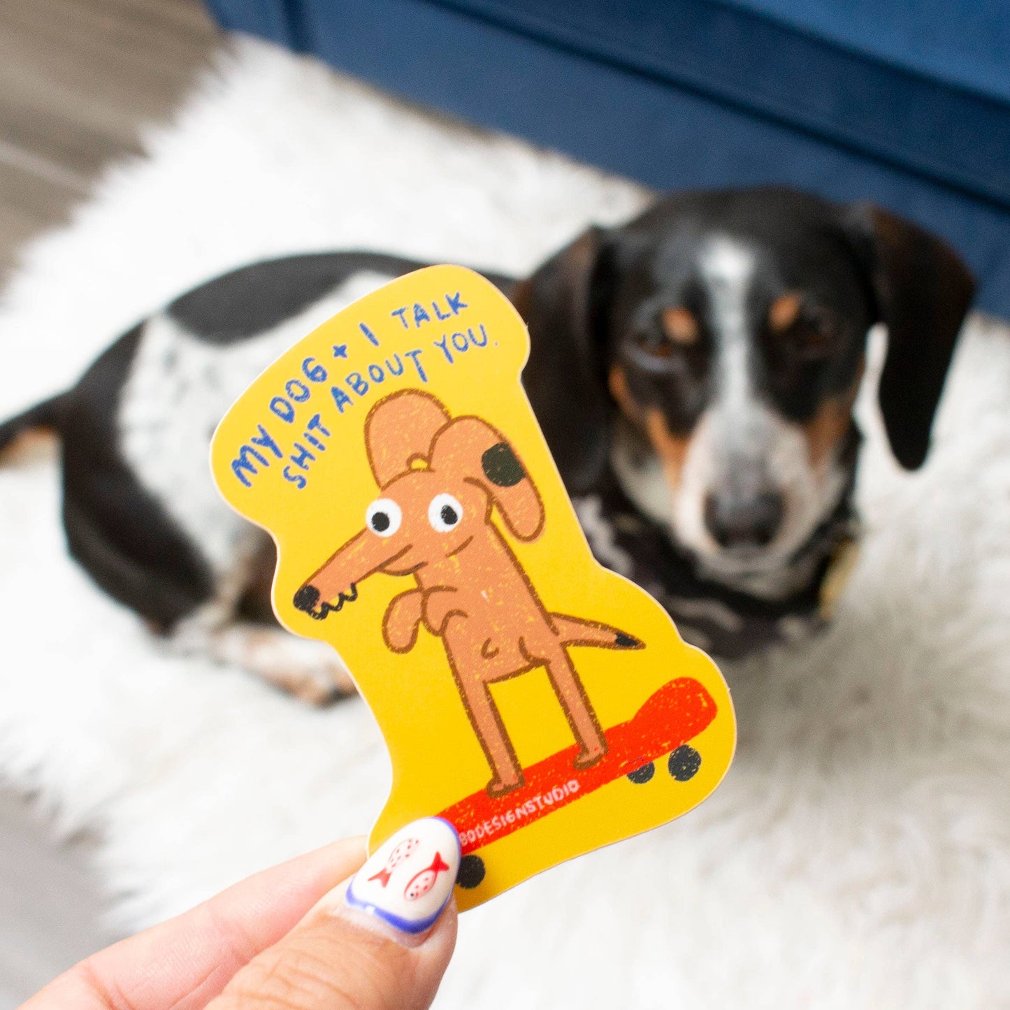 Dog toy with a cartoon dog design held by a hand, with a dog in the background.