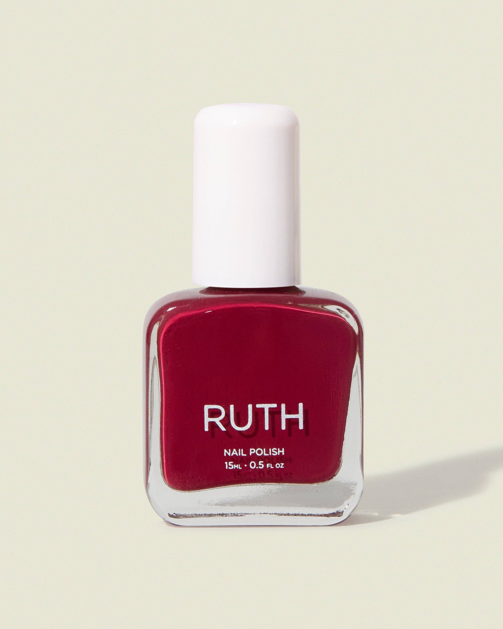 Red nail polish bottle with white cap on a beige background