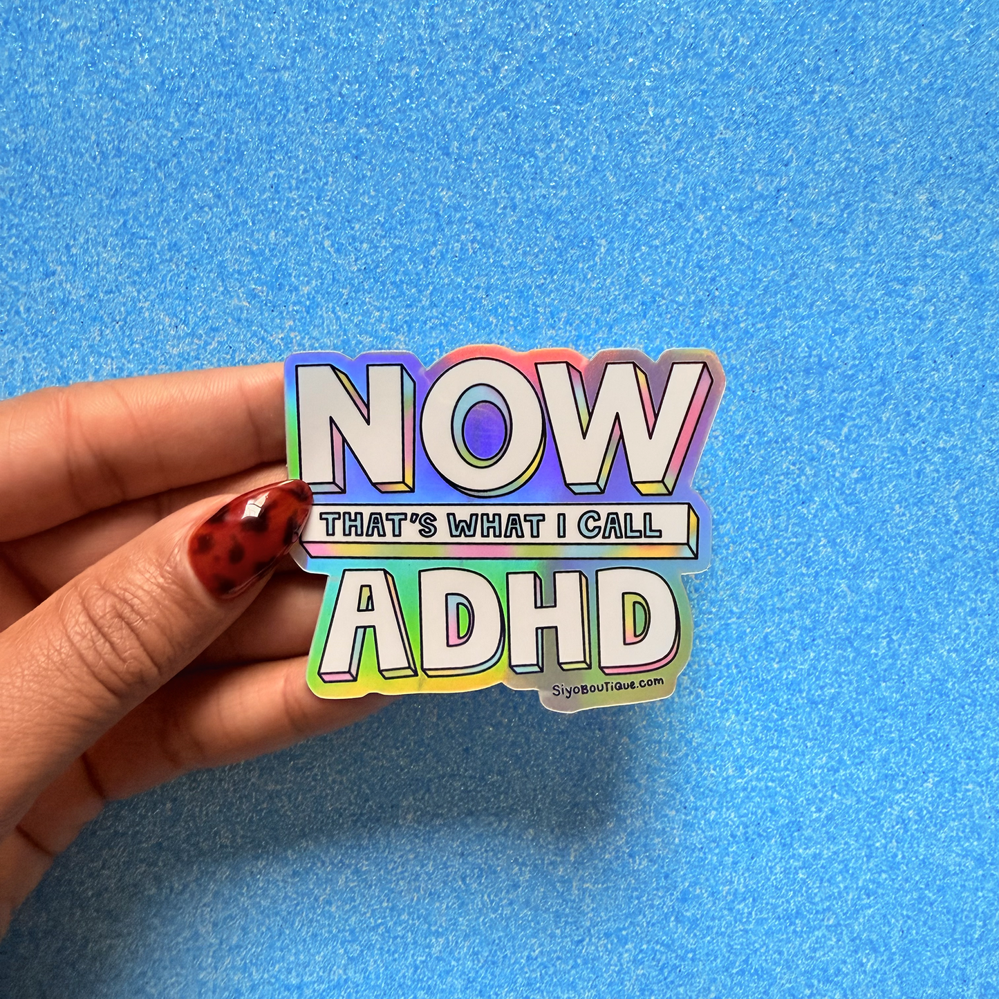 Hand holding a colorful sticker with 'NOW THAT'S WHAT I CALL ADHD' text on a blue background. Now Thats What I Call ADHD Holographic Sticker