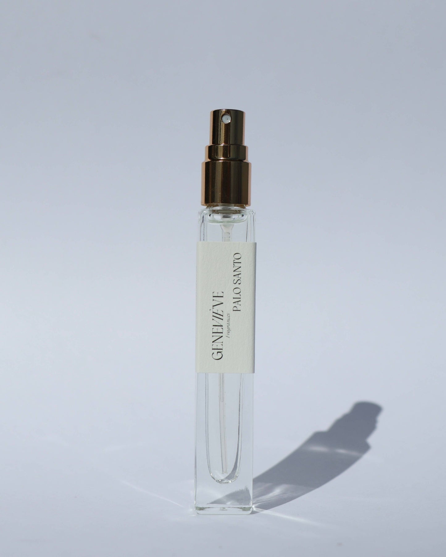 Clear spray bottle with gold cap on a light gray background