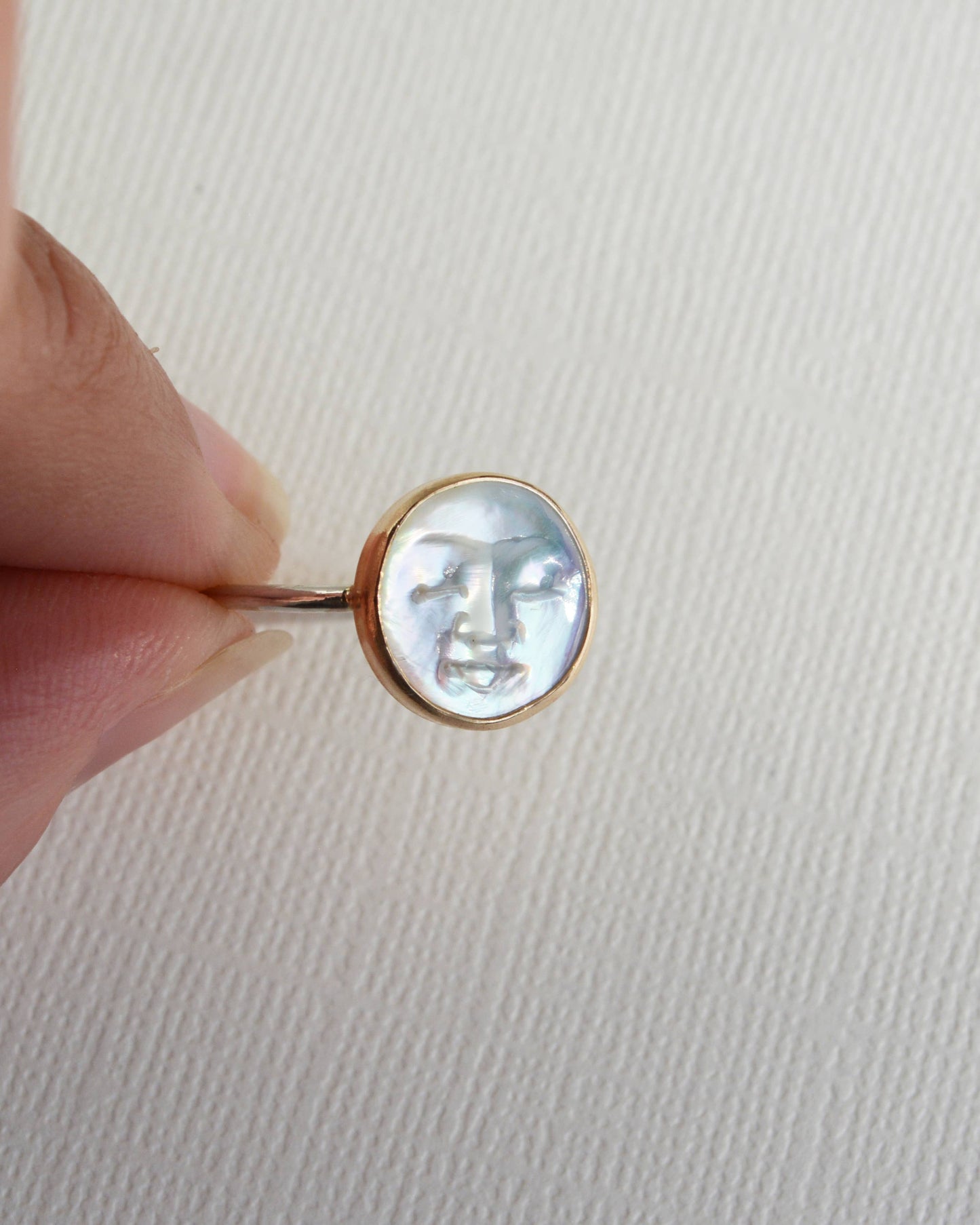 Close-up of a ring with a face design held by a hand on a light background, Pearl Moon Face Ring