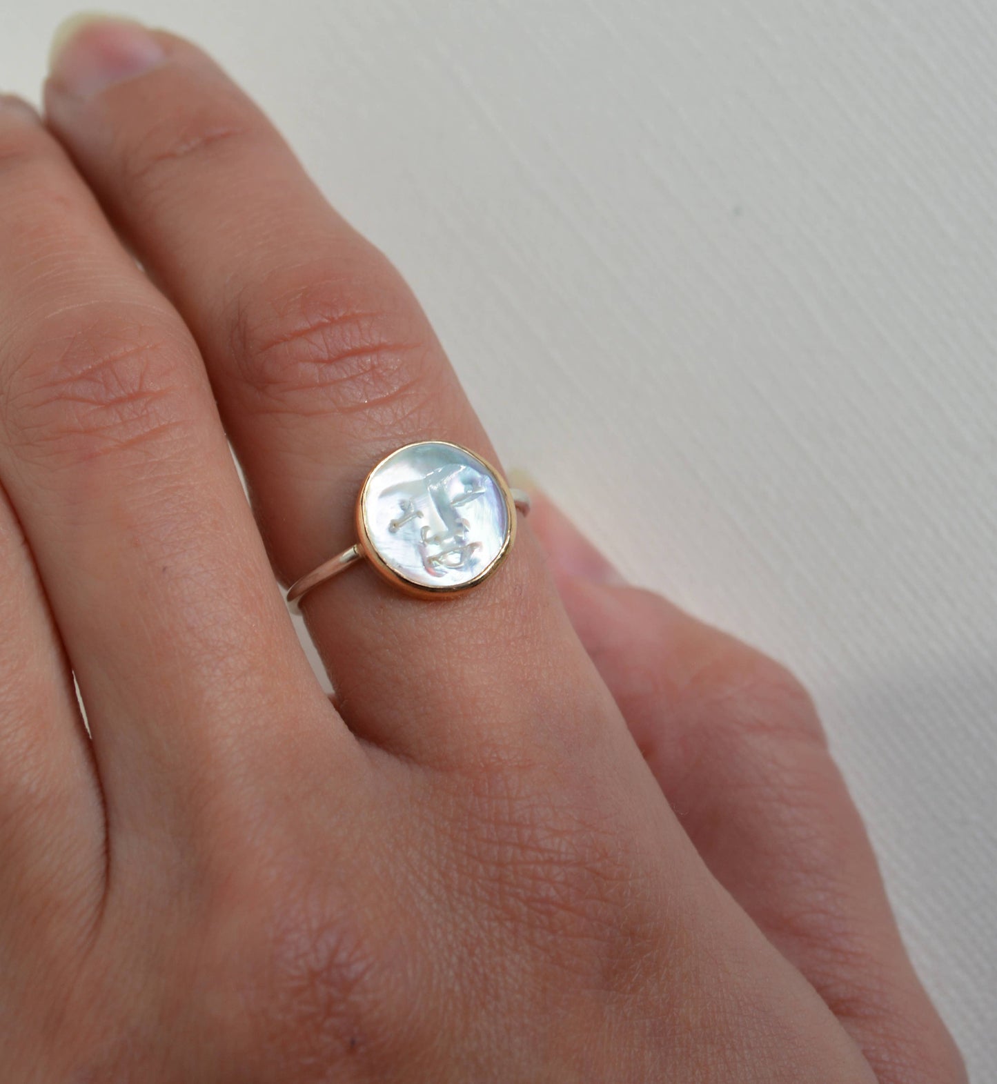 Gold ring with a circular stone on a person's finger against a plain, Pearl Moon Face Ringbackground
