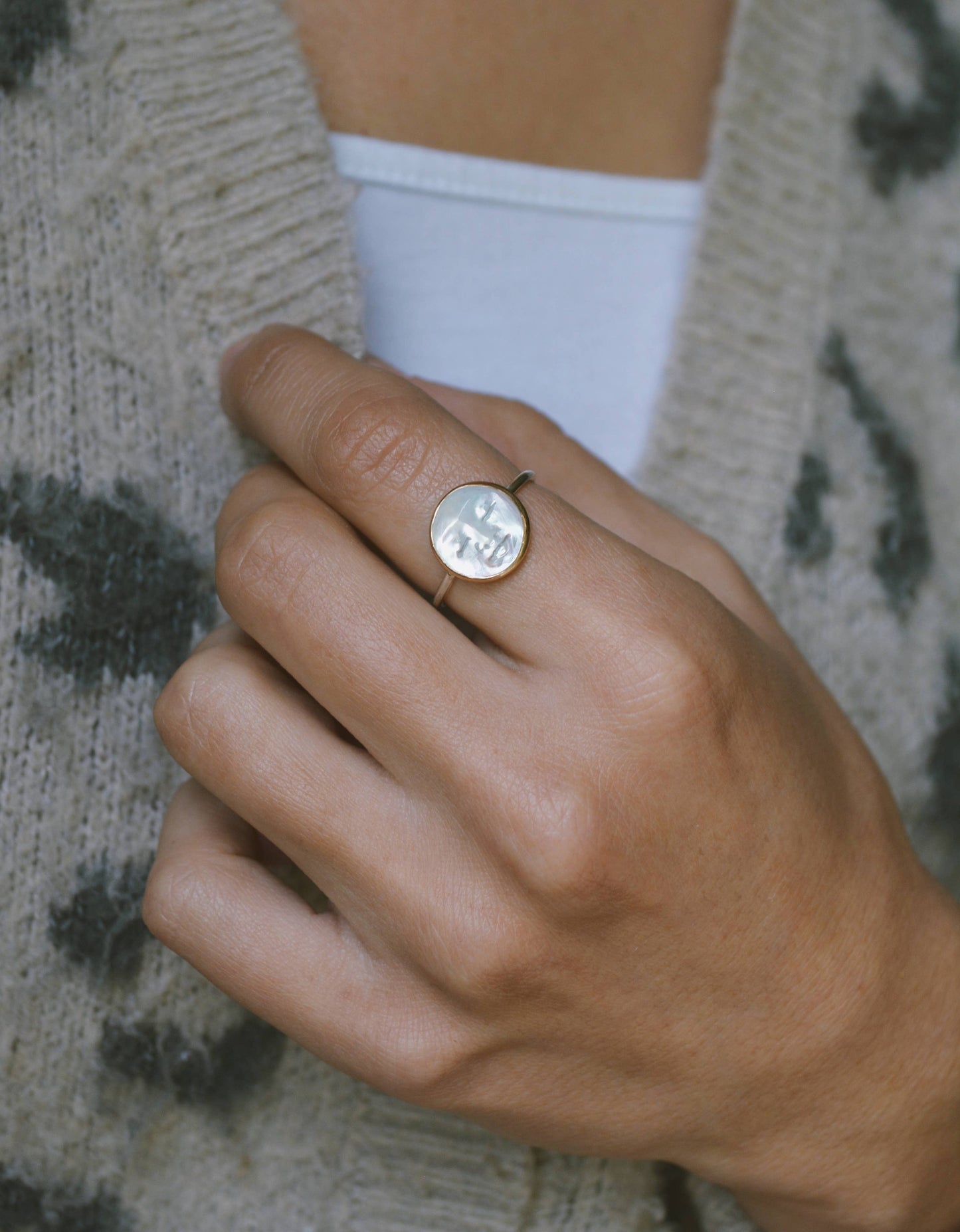 Close-up of a hand wearing a gold ring with a circular design, against a neutral background. Pearl Moon Face Ring