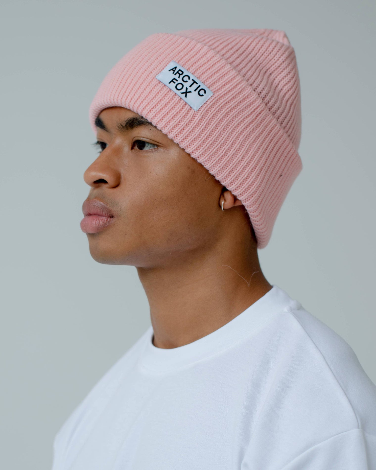 Person wearing a pink beanie with 'Arctic Fox' branding against a plain, Pink Recycled Bottle Beaniebackground