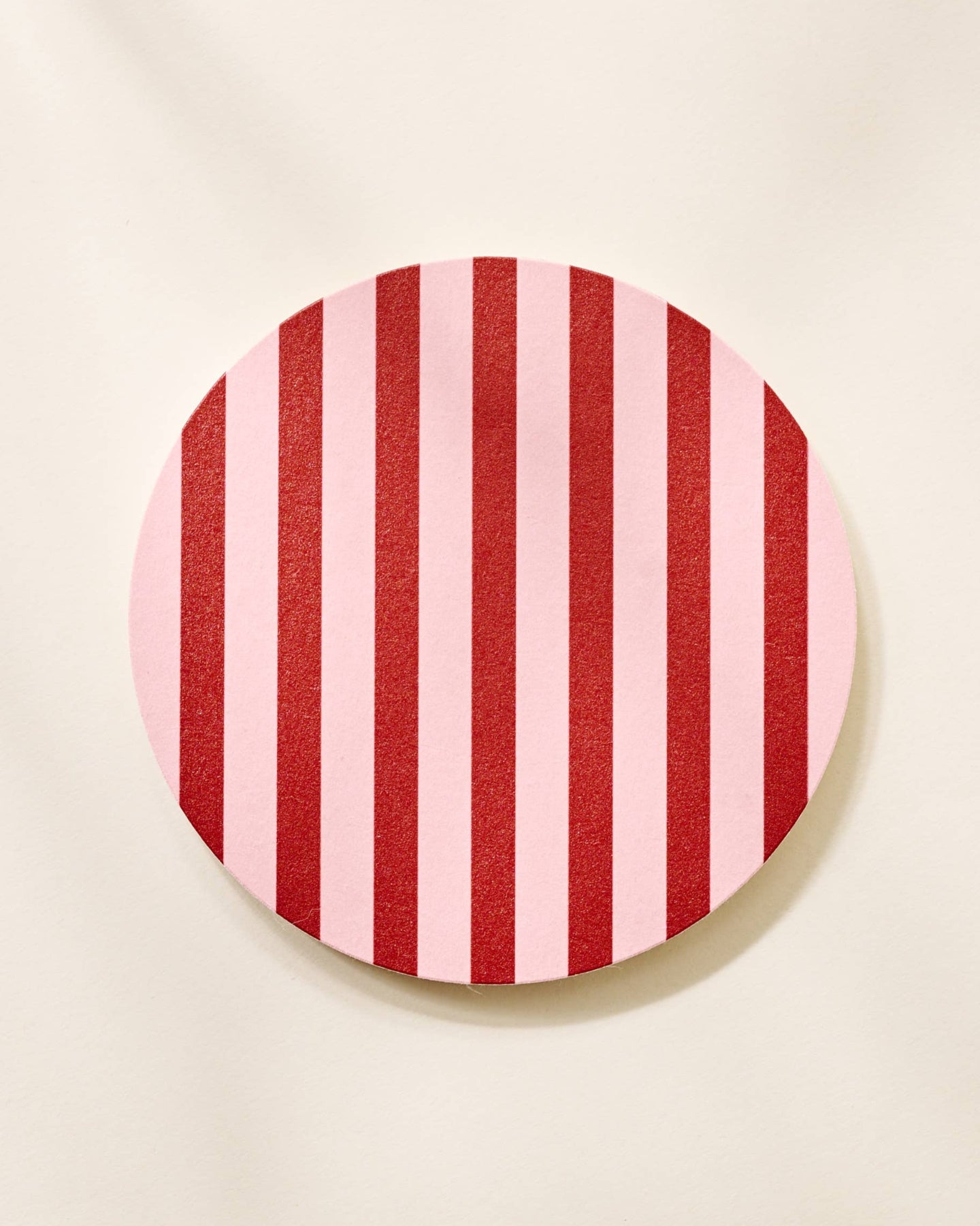 Round red and pink striped coaster on a beige background