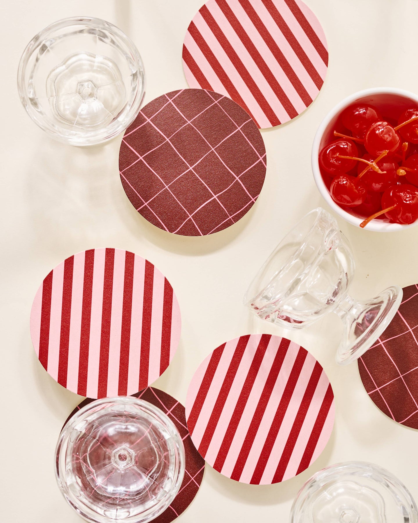 Red and white striped coasters on a light surface with glasses and cherries.