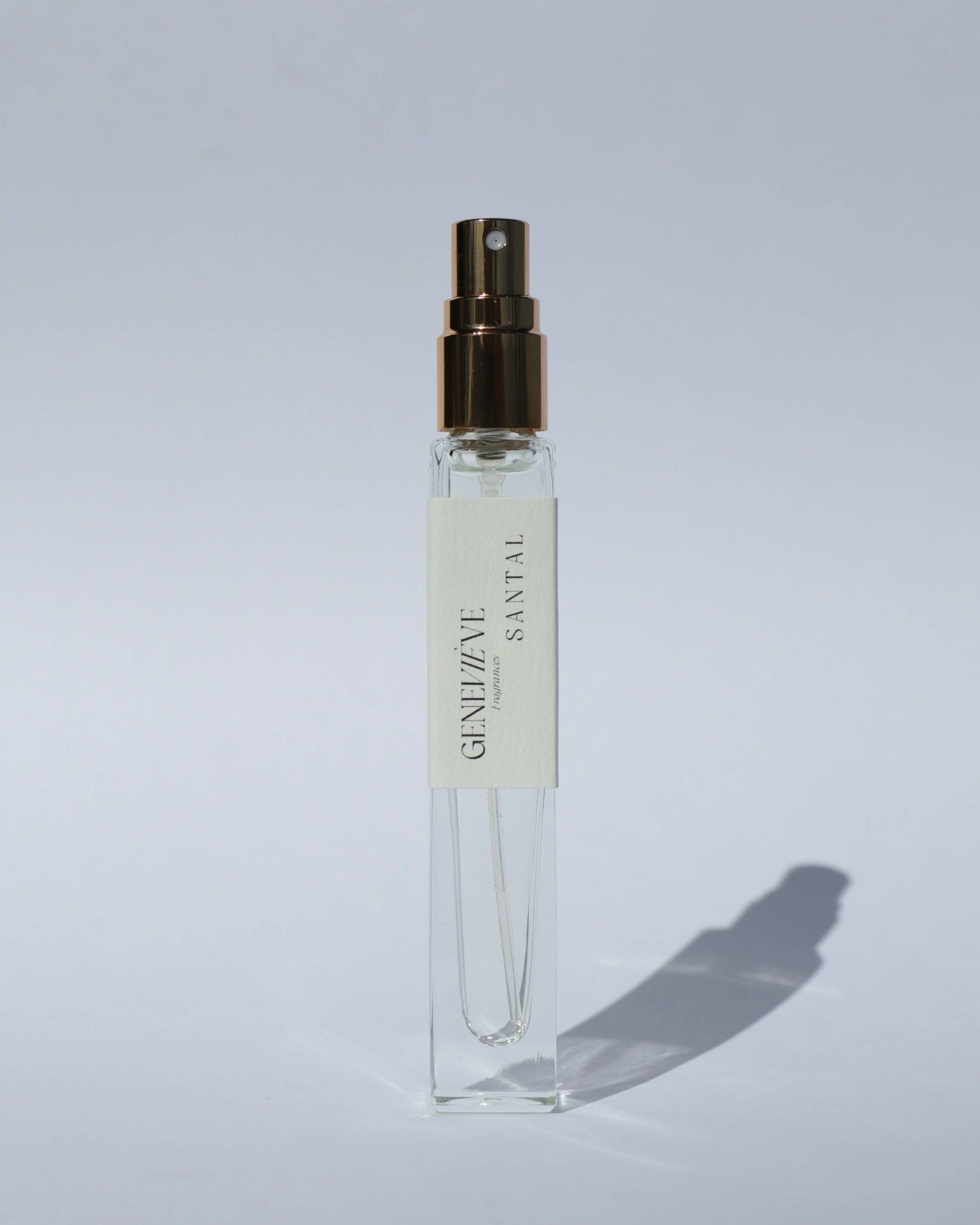 Small clear spray bottle with a gold cap on a light gray background