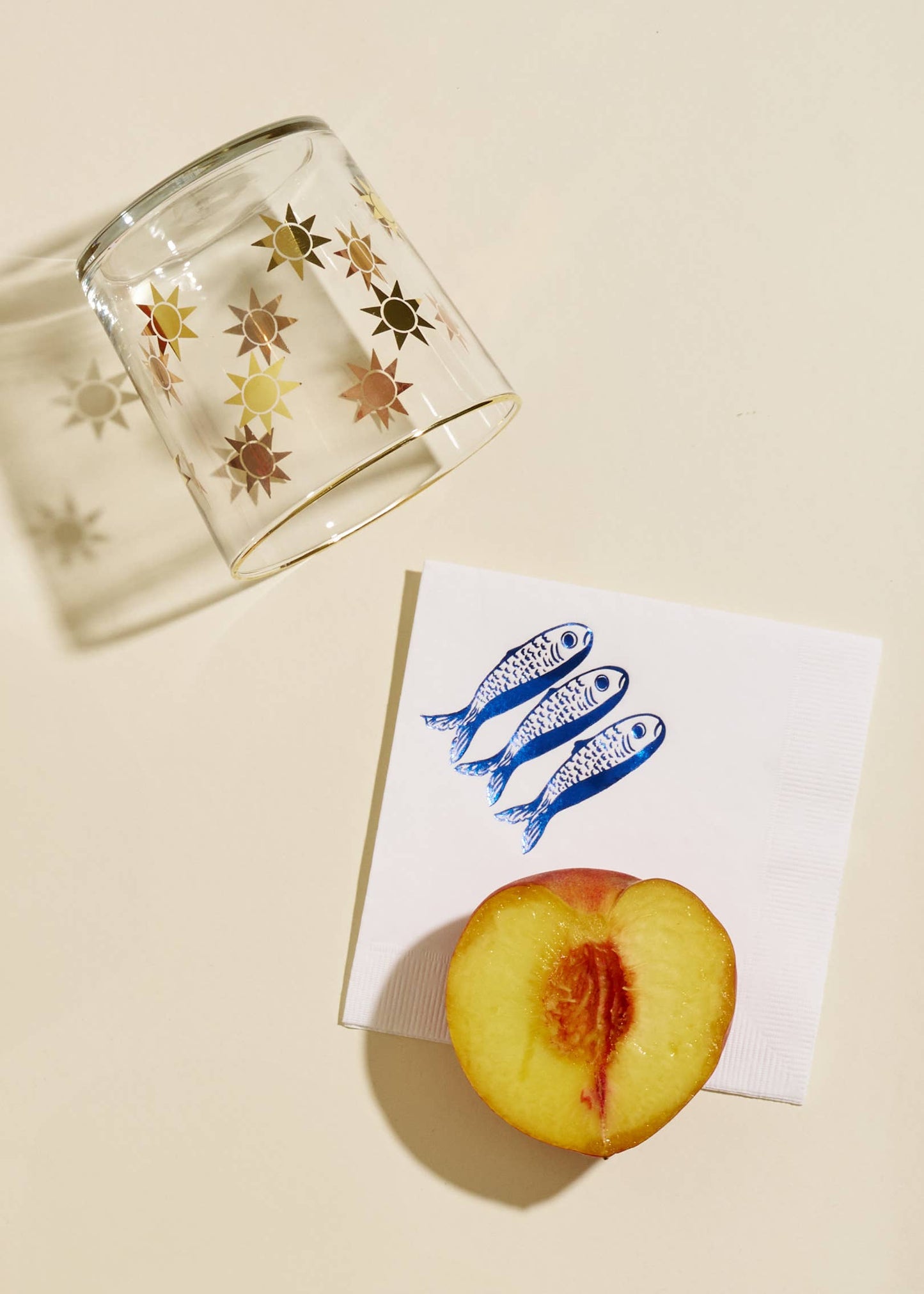 Clear glass with star designs, a folded card with blue fish illustration, and a peach half on a beige surface.