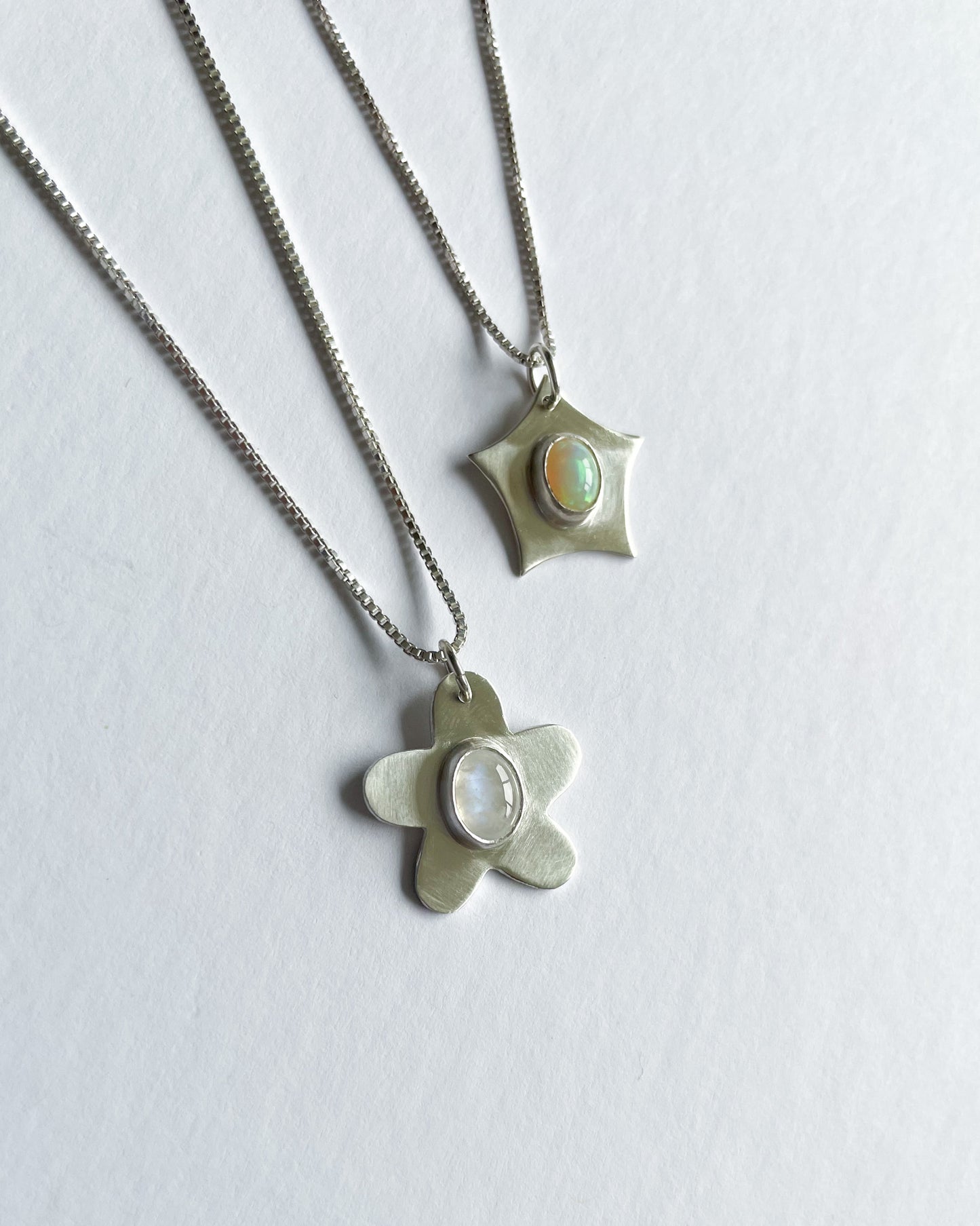 Two silver pendants with opal stones on a white background