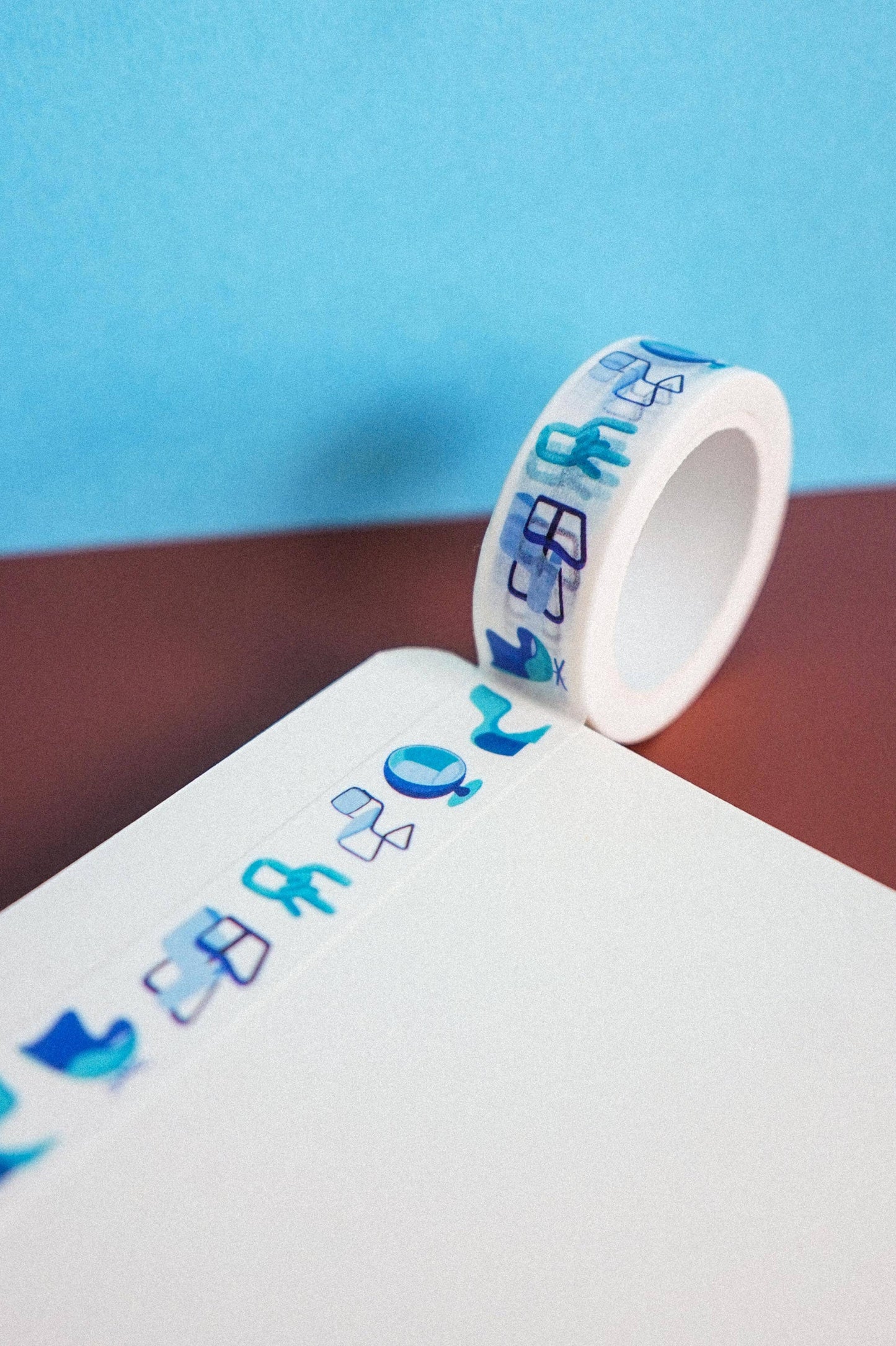 Roll of decorative tape with blue designs on a white surface against a blue background