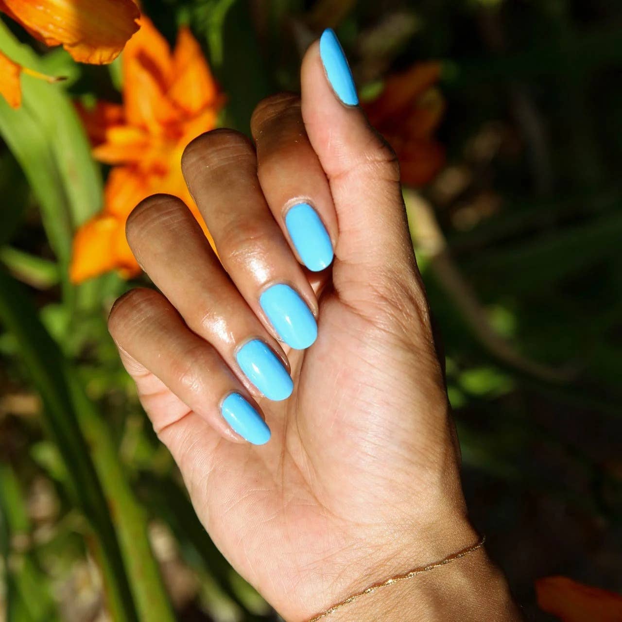 Hand with blue nail polish in front of orange flowers