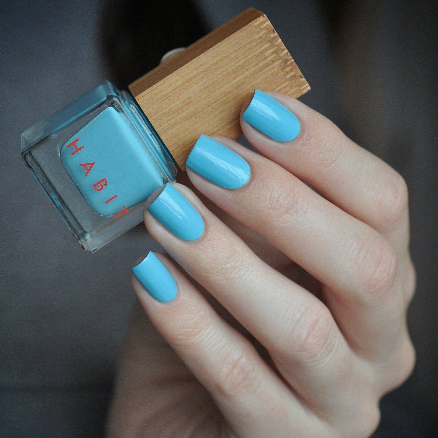 Hand with blue nail polish holding a bottle of Habit nail polish.