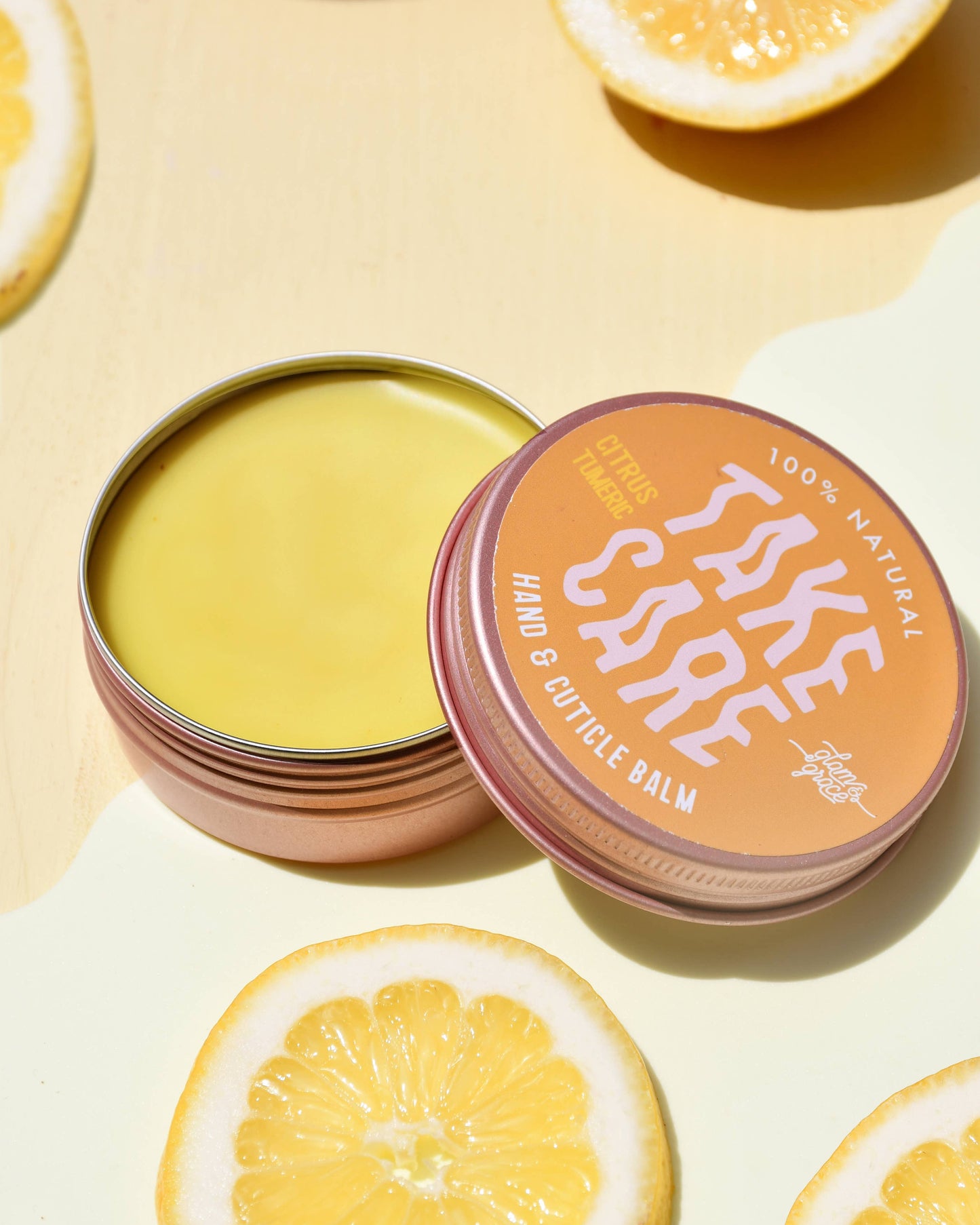 Hand and cuticle balm with a decorative lid on a yellow background with lemon slices.