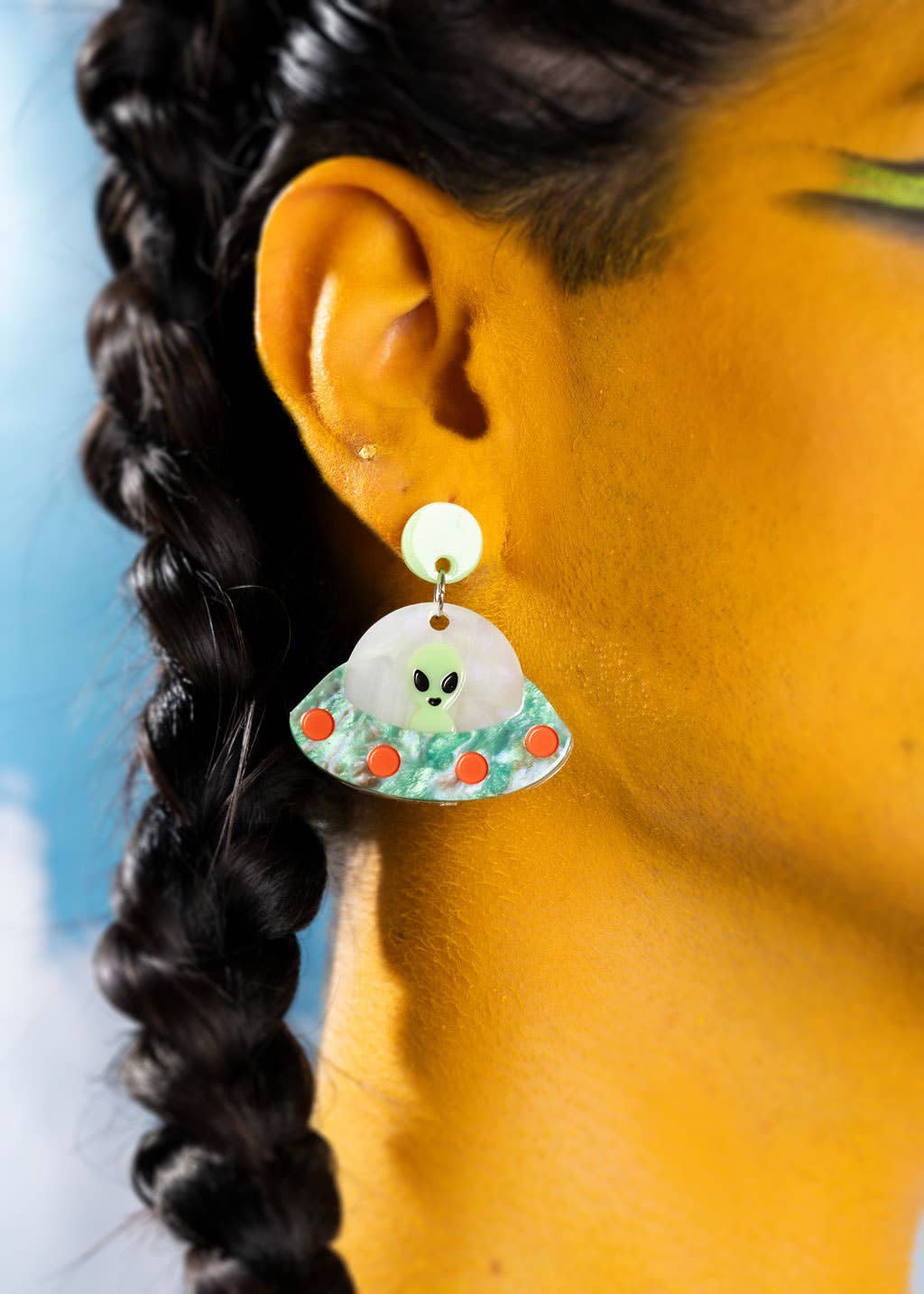 Close-up of an ear wearing a unique earrings with a UFO design, against a blurred background.