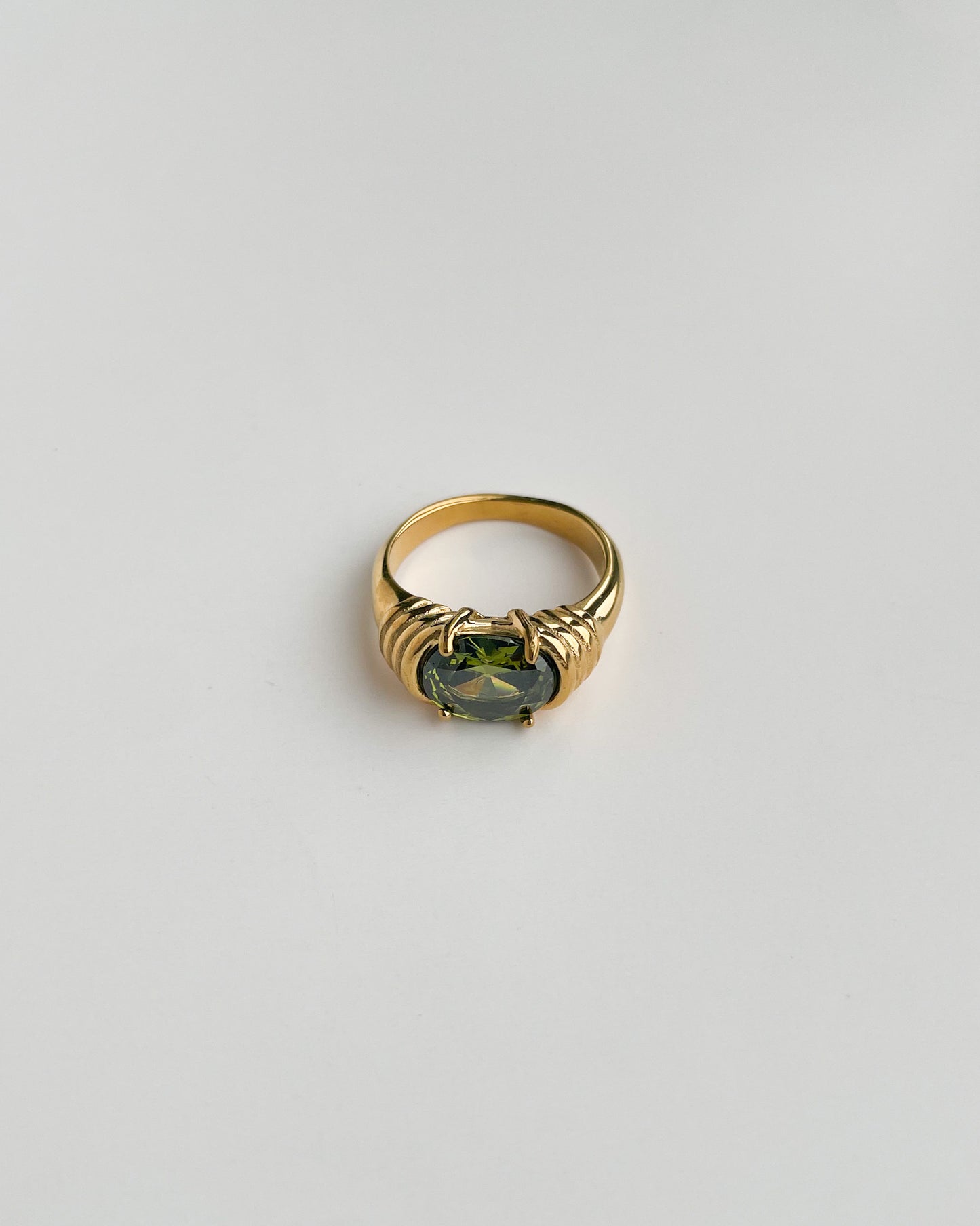 Gold ring with a green gemstone on a light gray background
