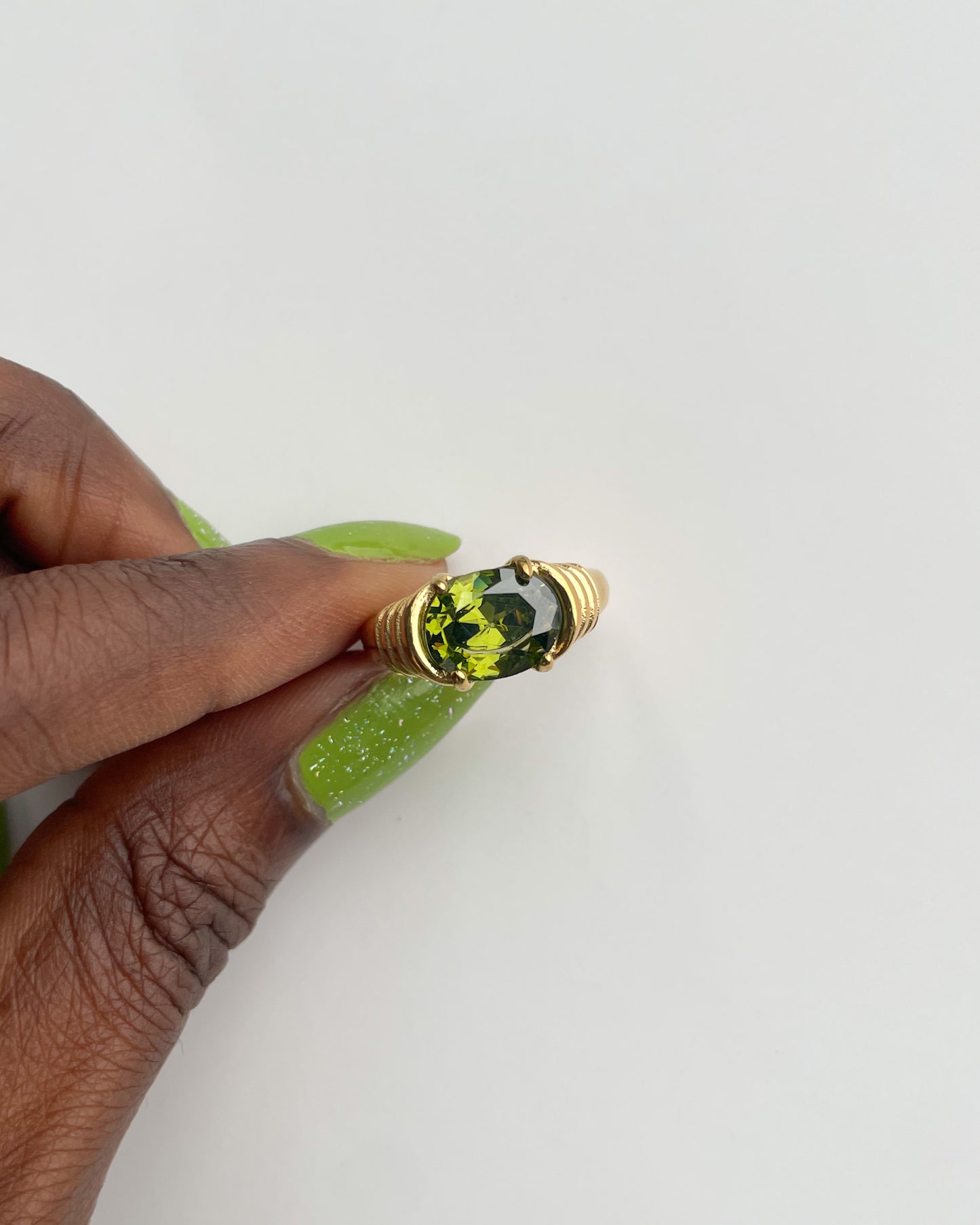 Gold ring with a green gemstone held by a hand on a white background